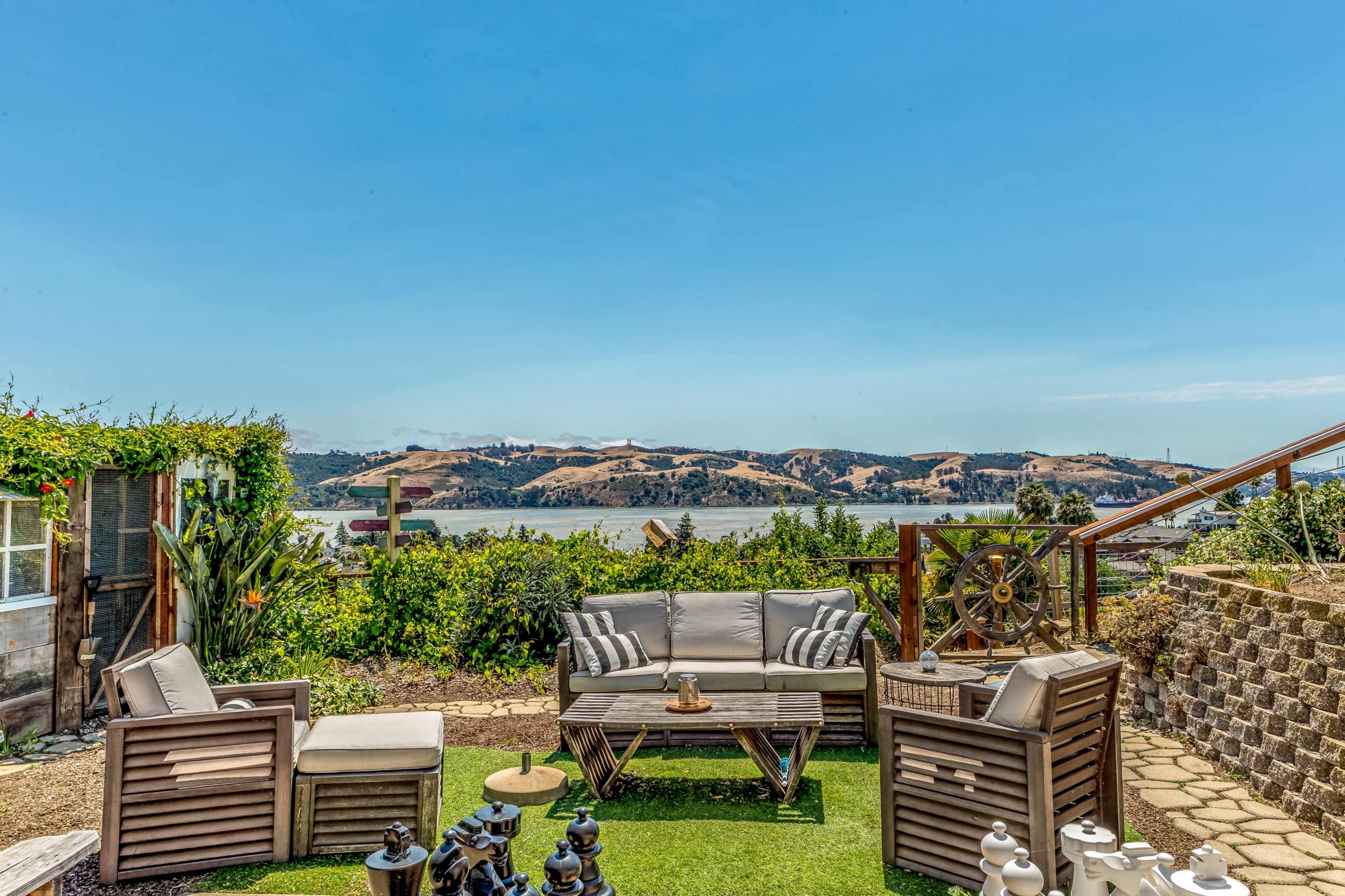 A seating area with a sofa and chairs overlooks a body of water and rolling hills in the distance.