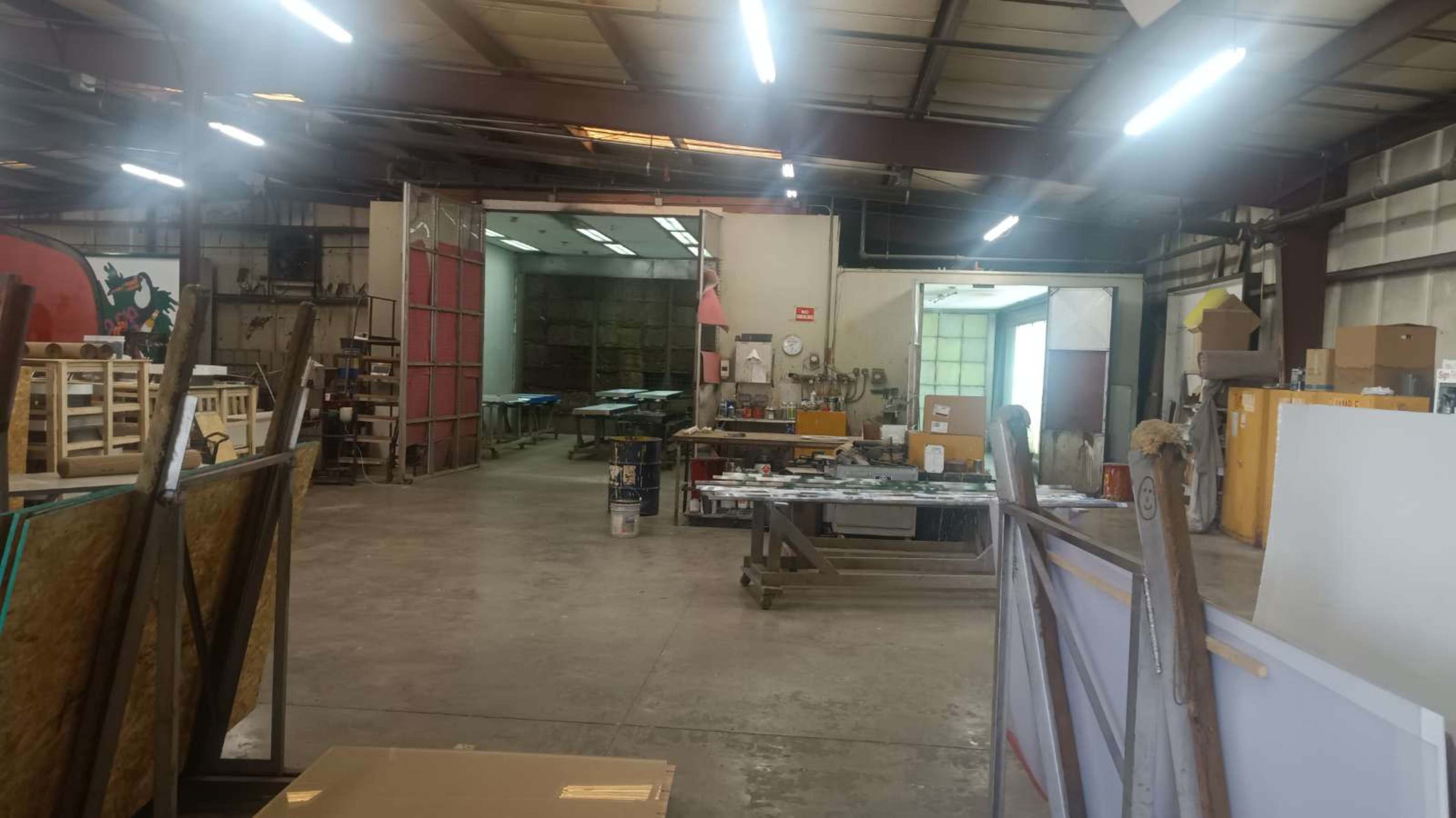 The image shows a spacious workshop or manufacturing area with open work tables, shelves, and tools arranged throughout the space.