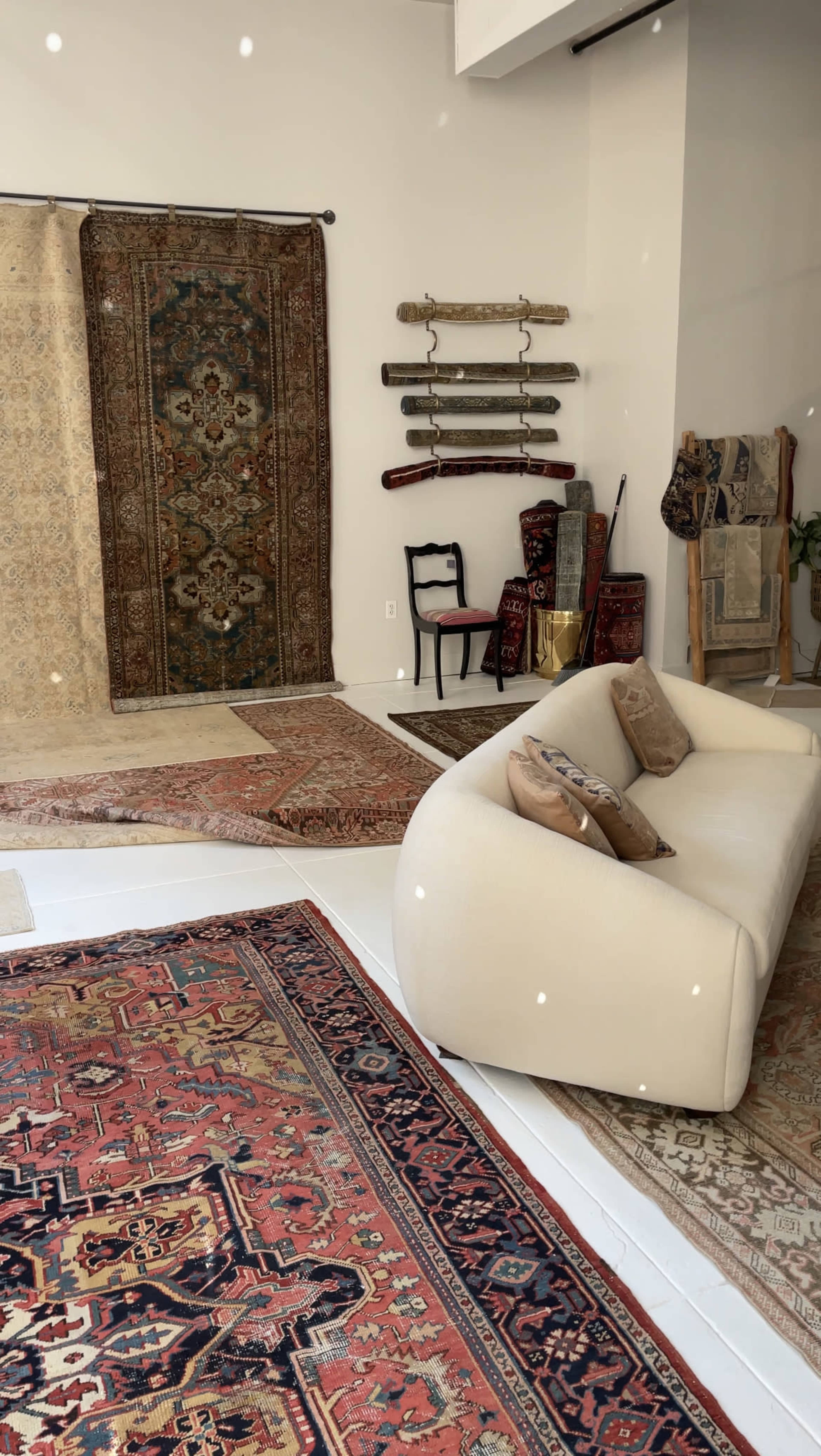 A light-colored modern sofa in a room with various area rugs, wall hangings, and decorative objects, creating an eclectic interior space.