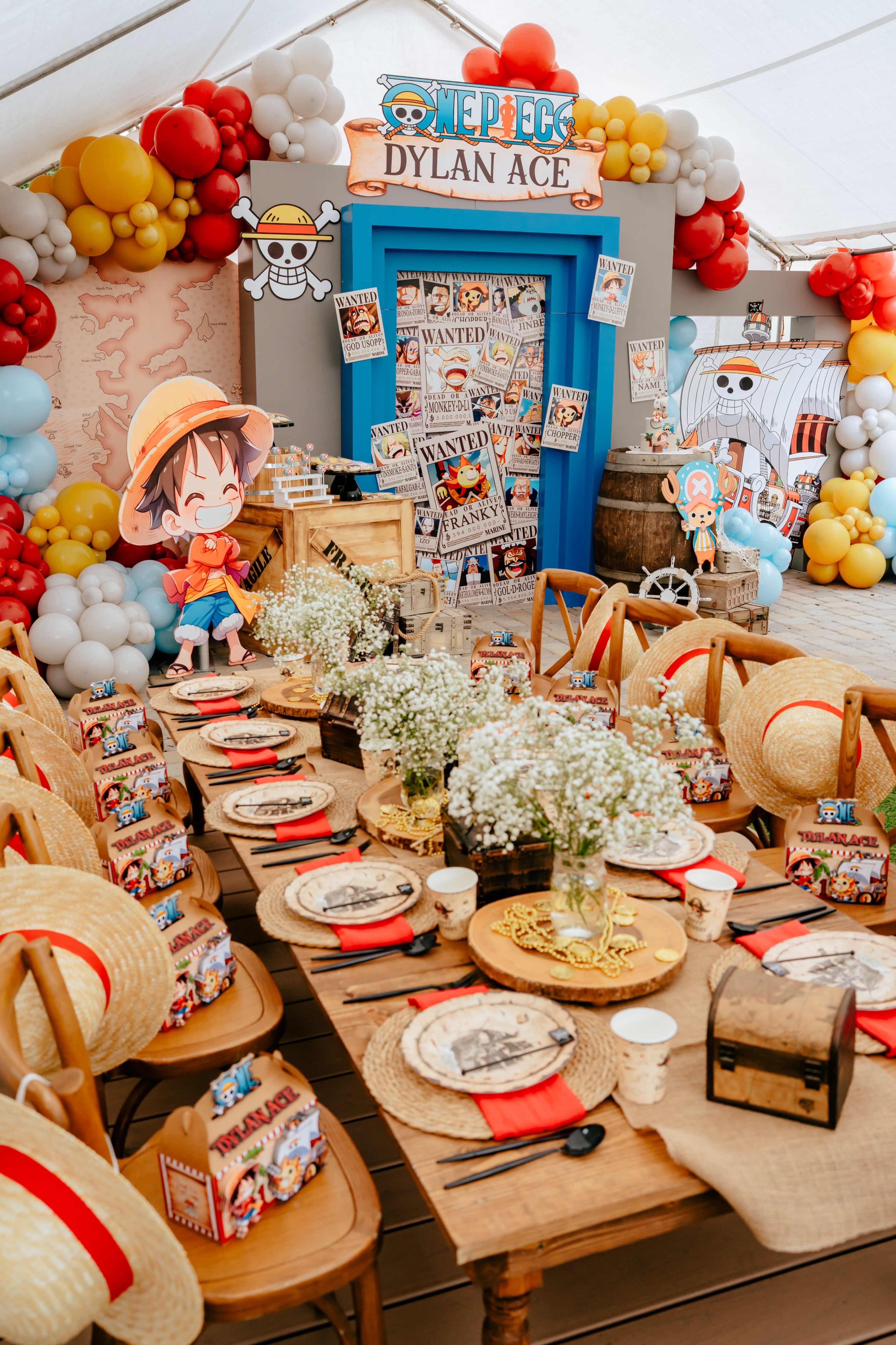 A colorful birthday party setup features a long table adorned with plates and decorations, with a backdrop displaying a "One Piece" theme and character cutouts.
