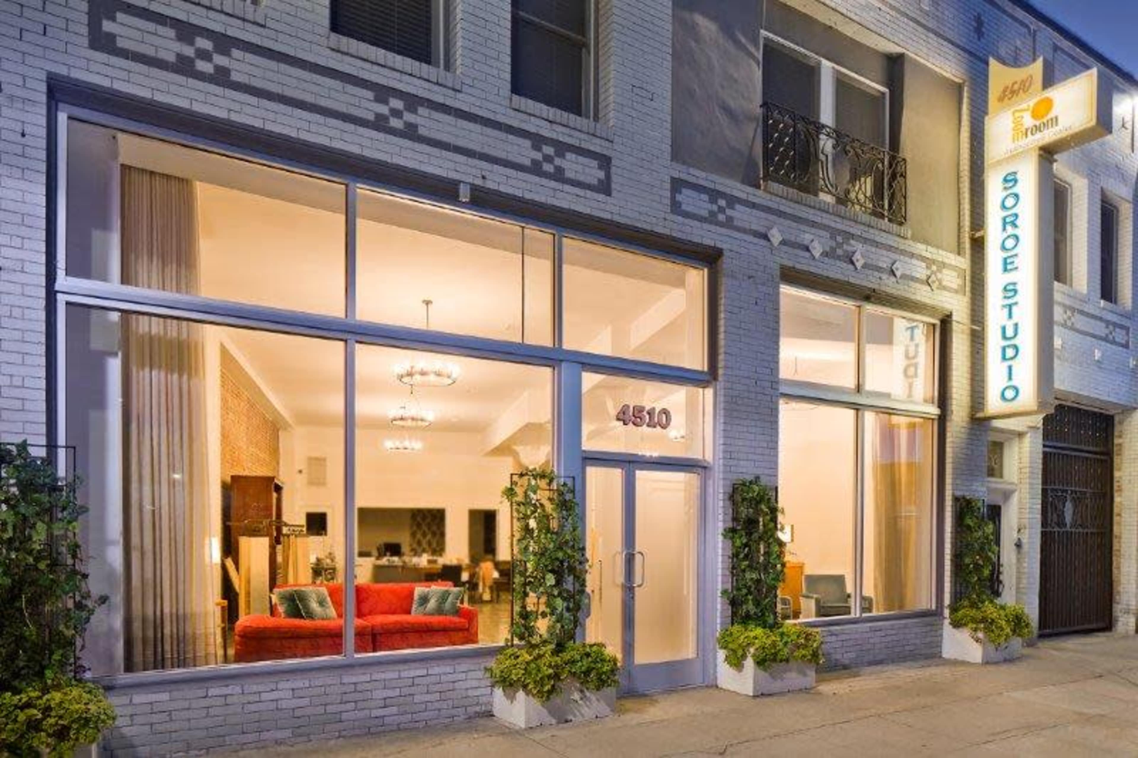 The image shows a building with large windows displaying a well-lit interior that features a red couch, with the establishment's name "Soro Studio" illuminated on the side.