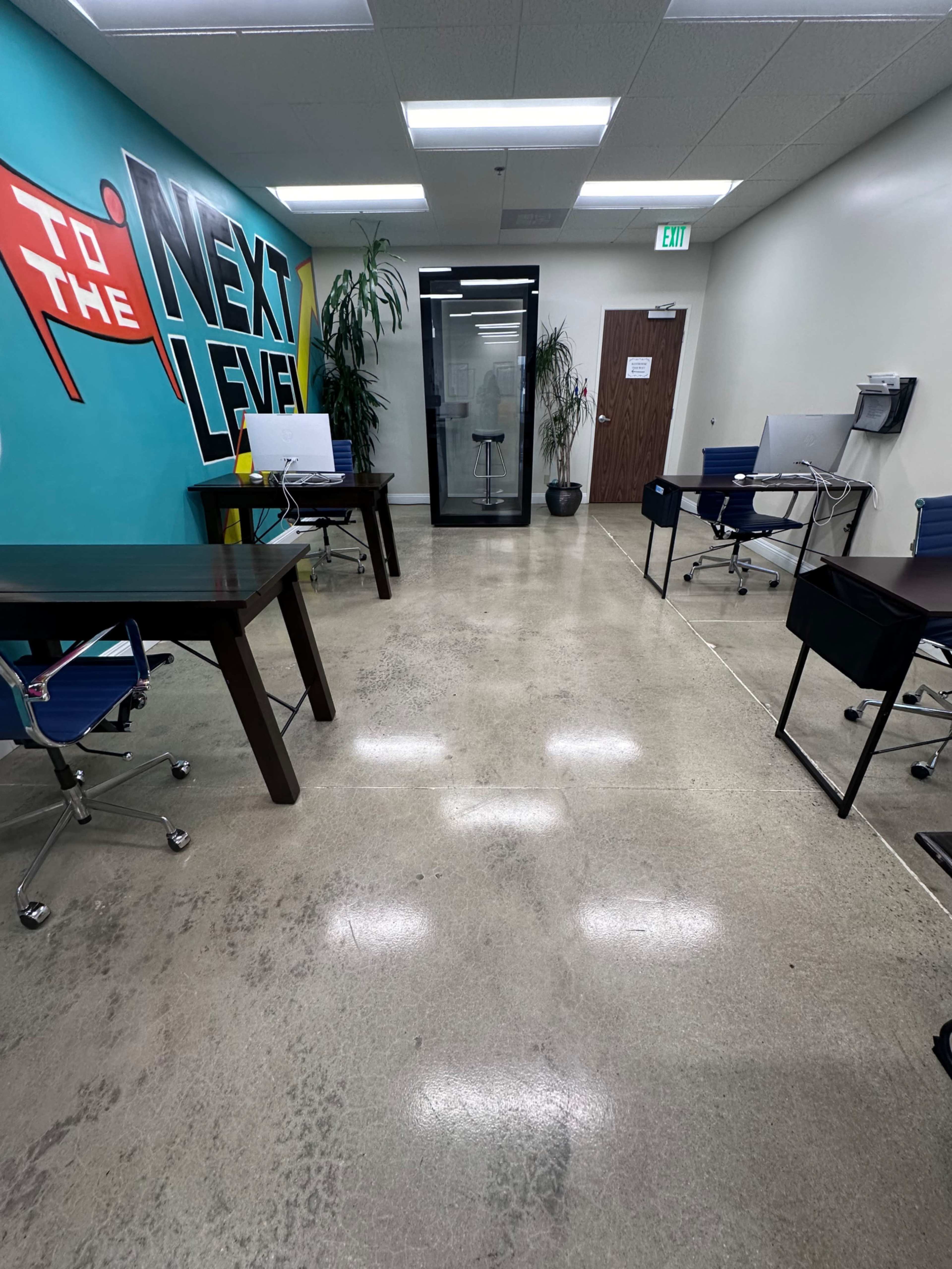 A modern office space with a polished concrete floor, featuring several desks and a glass-enclosed meeting room in the background.