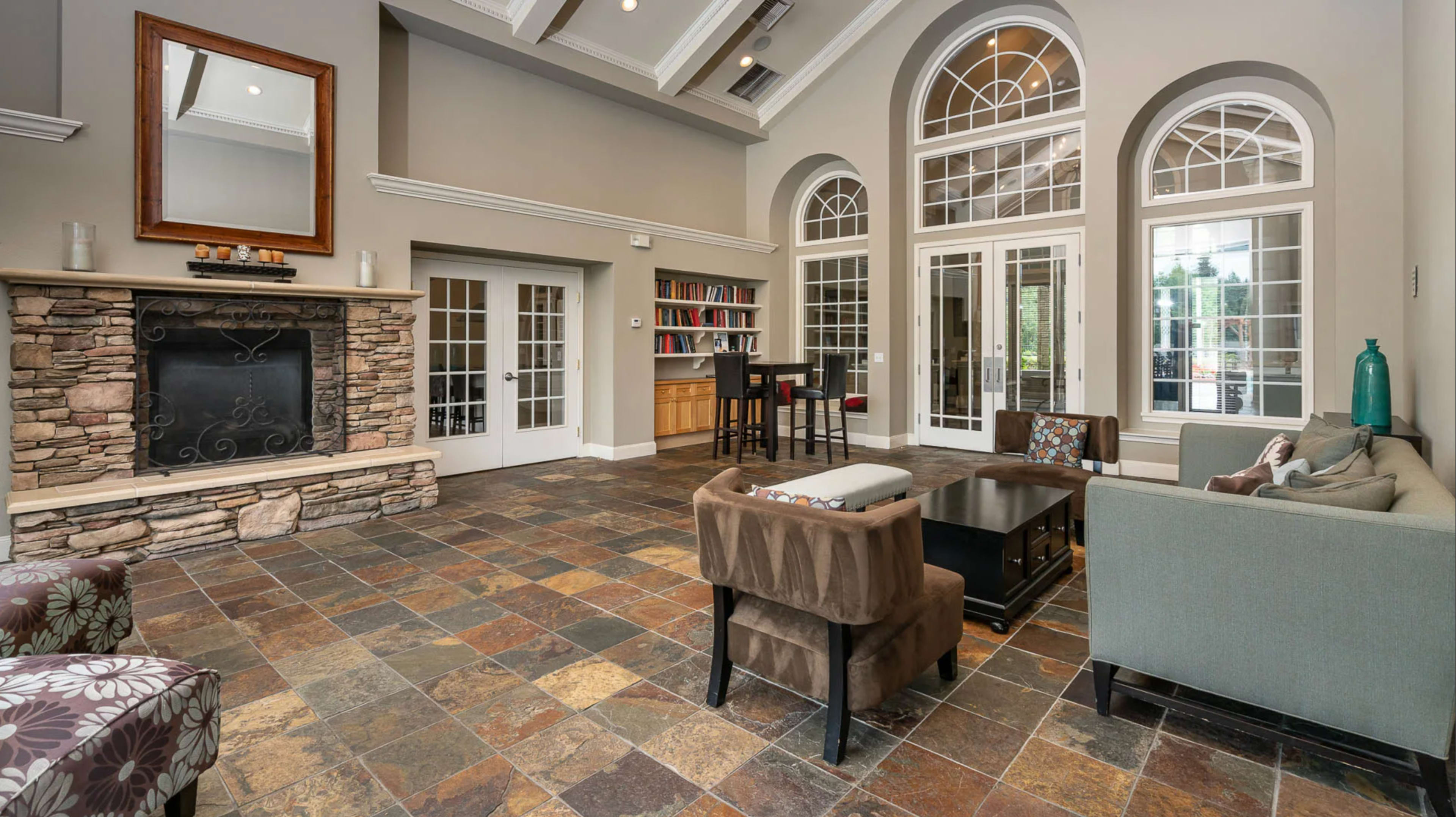 The room features a stone fireplace, large arched windows, and a seating area with a coffee table and bookshelves.