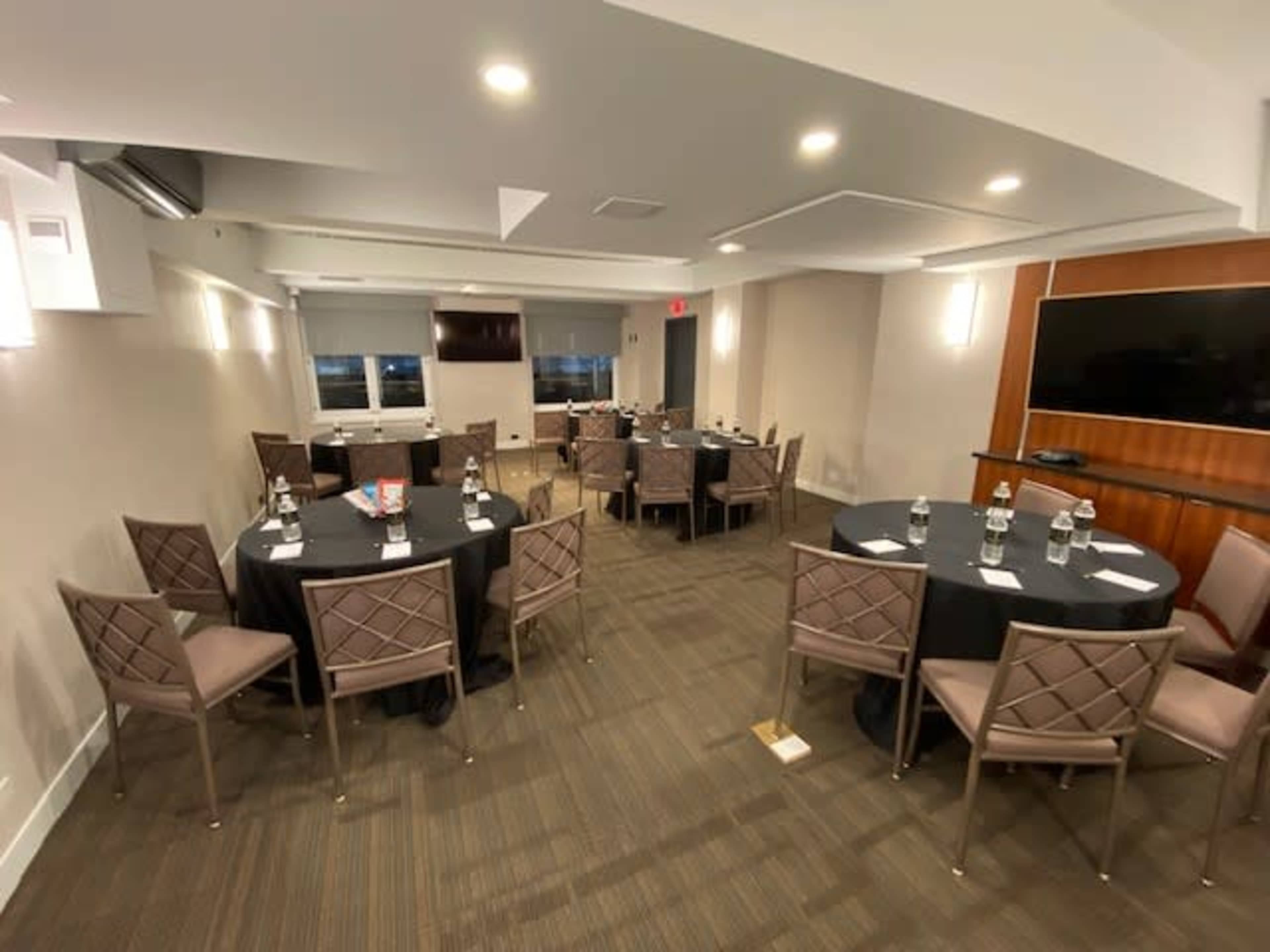 A conference room arranged with several round tables set for a meeting, featuring bottles of water and pens at each place.