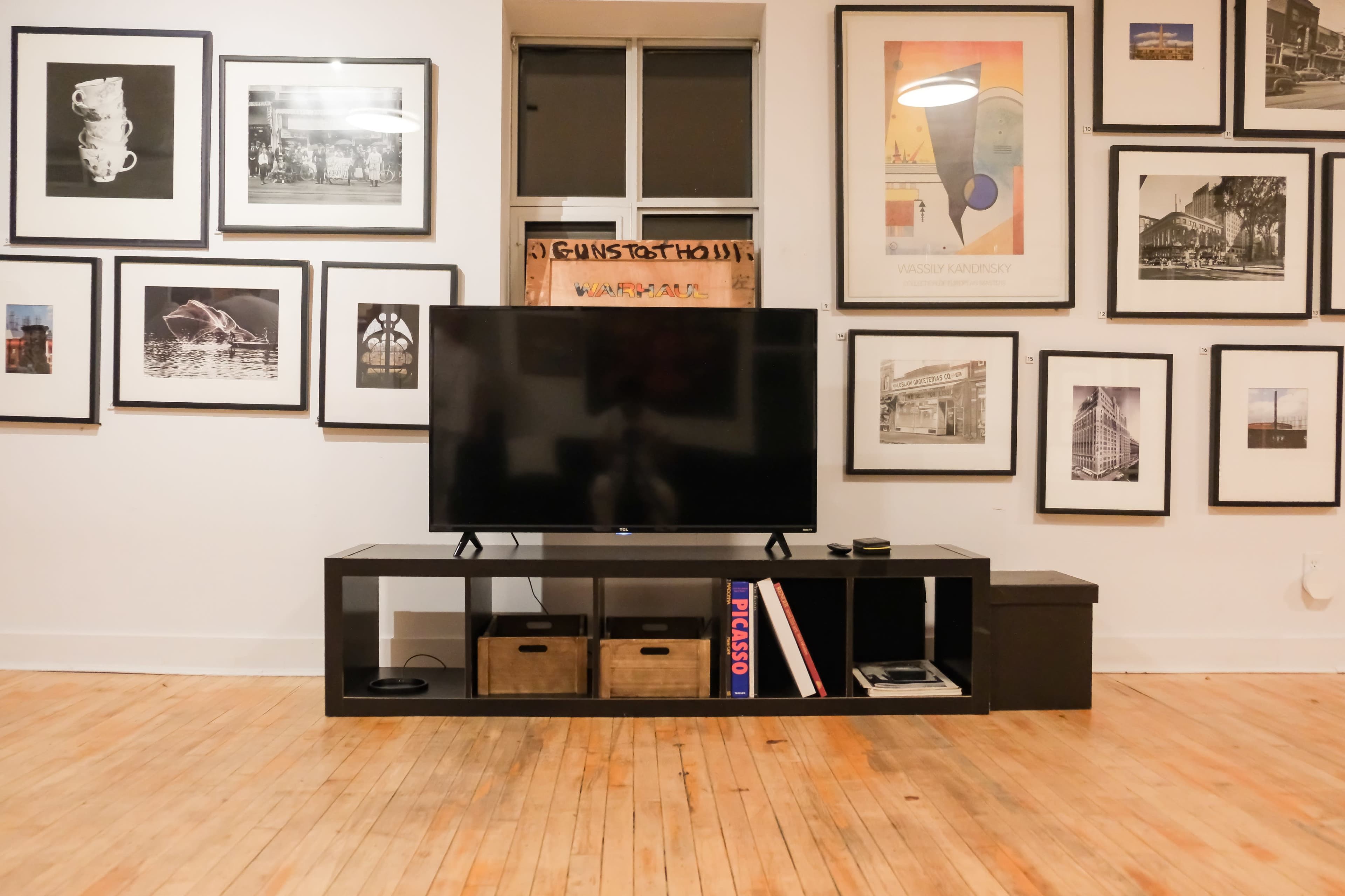 A flat-screen television is placed on a low shelf in front of a wall covered with framed black-and-white photographs and artwork.
