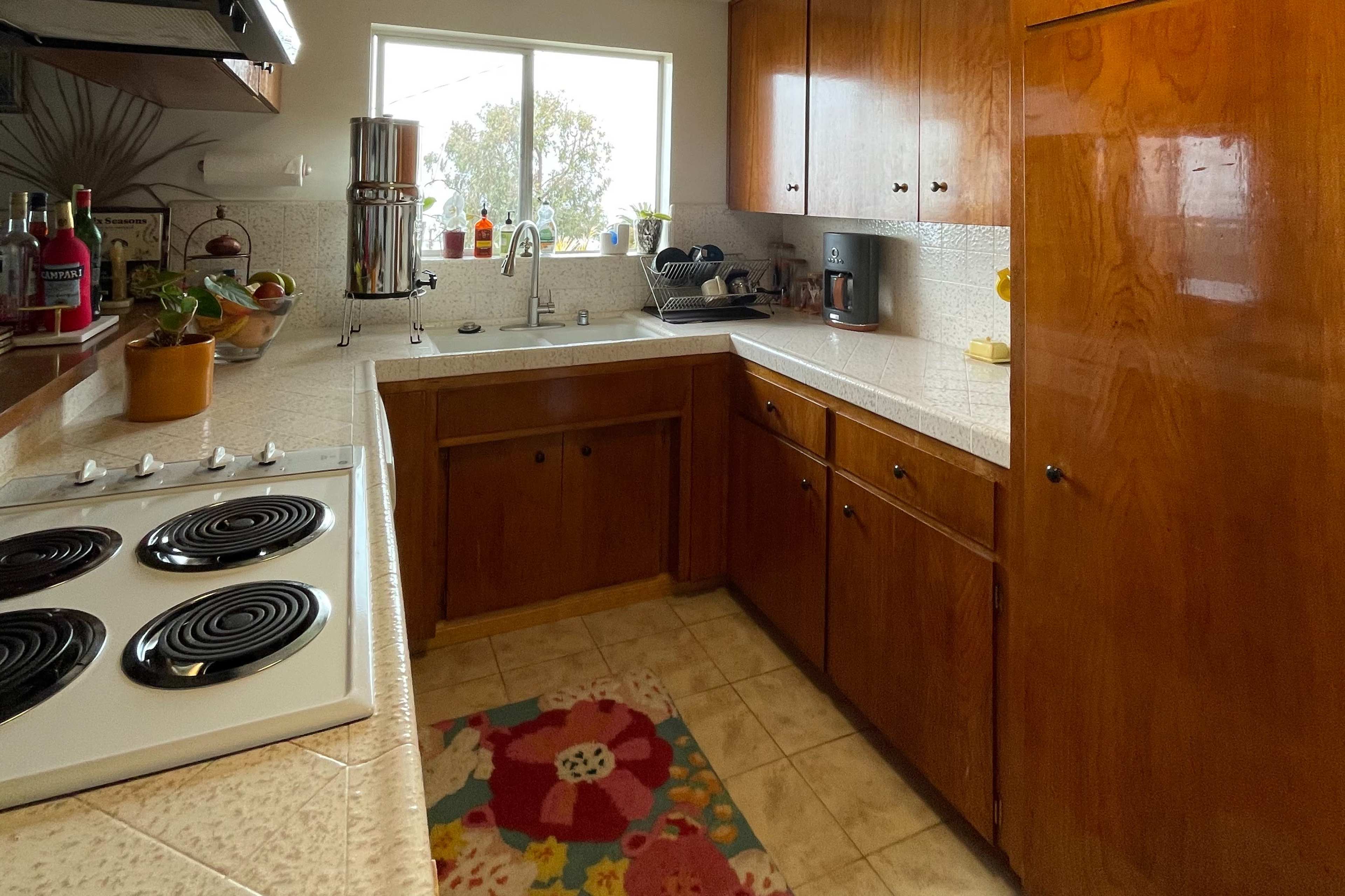 A compact kitchen with wooden cabinets, a sink under a window, and a stove with black burners.