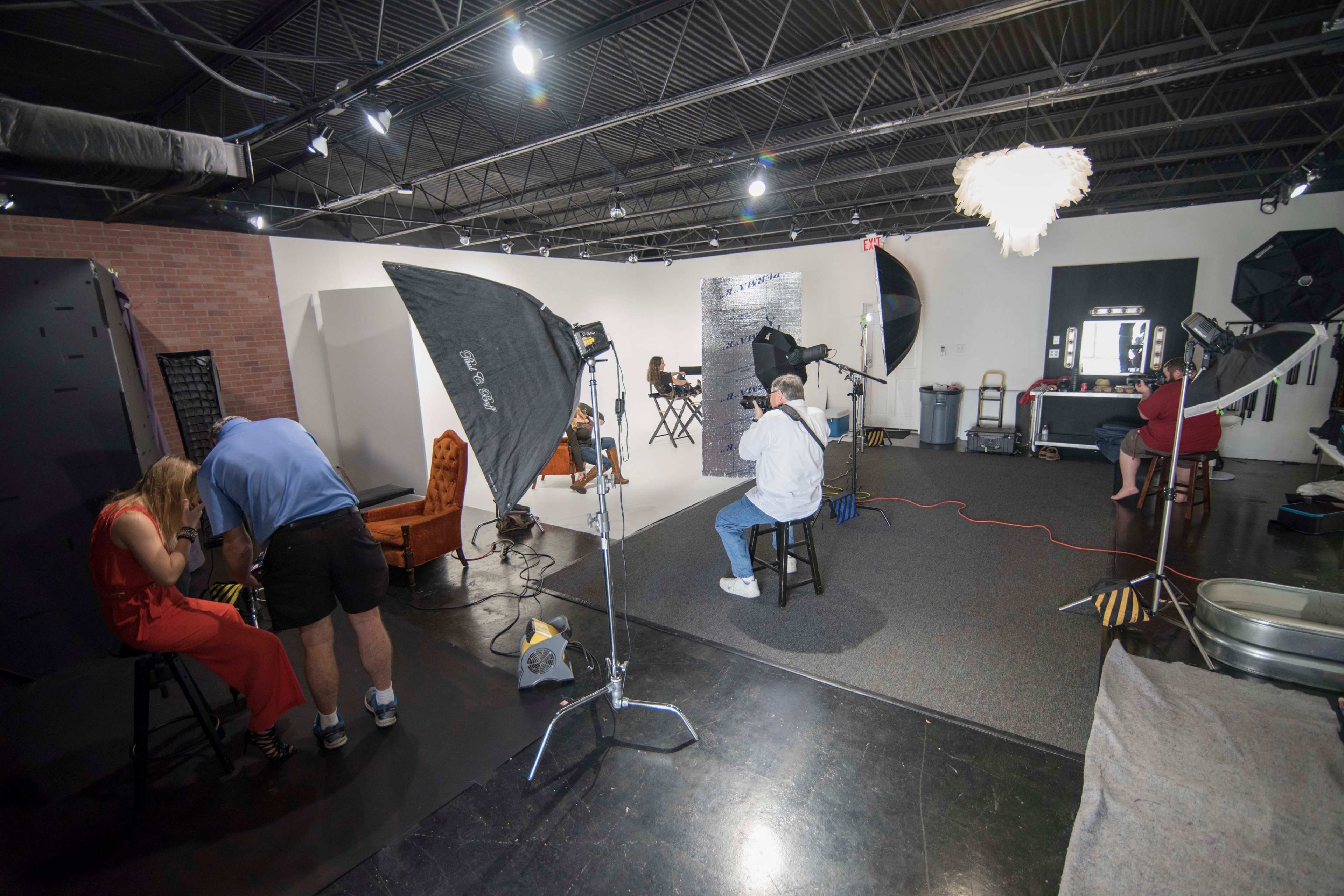 A photography studio features various setups with photographers capturing subjects in different areas, illuminated by multiple lights.