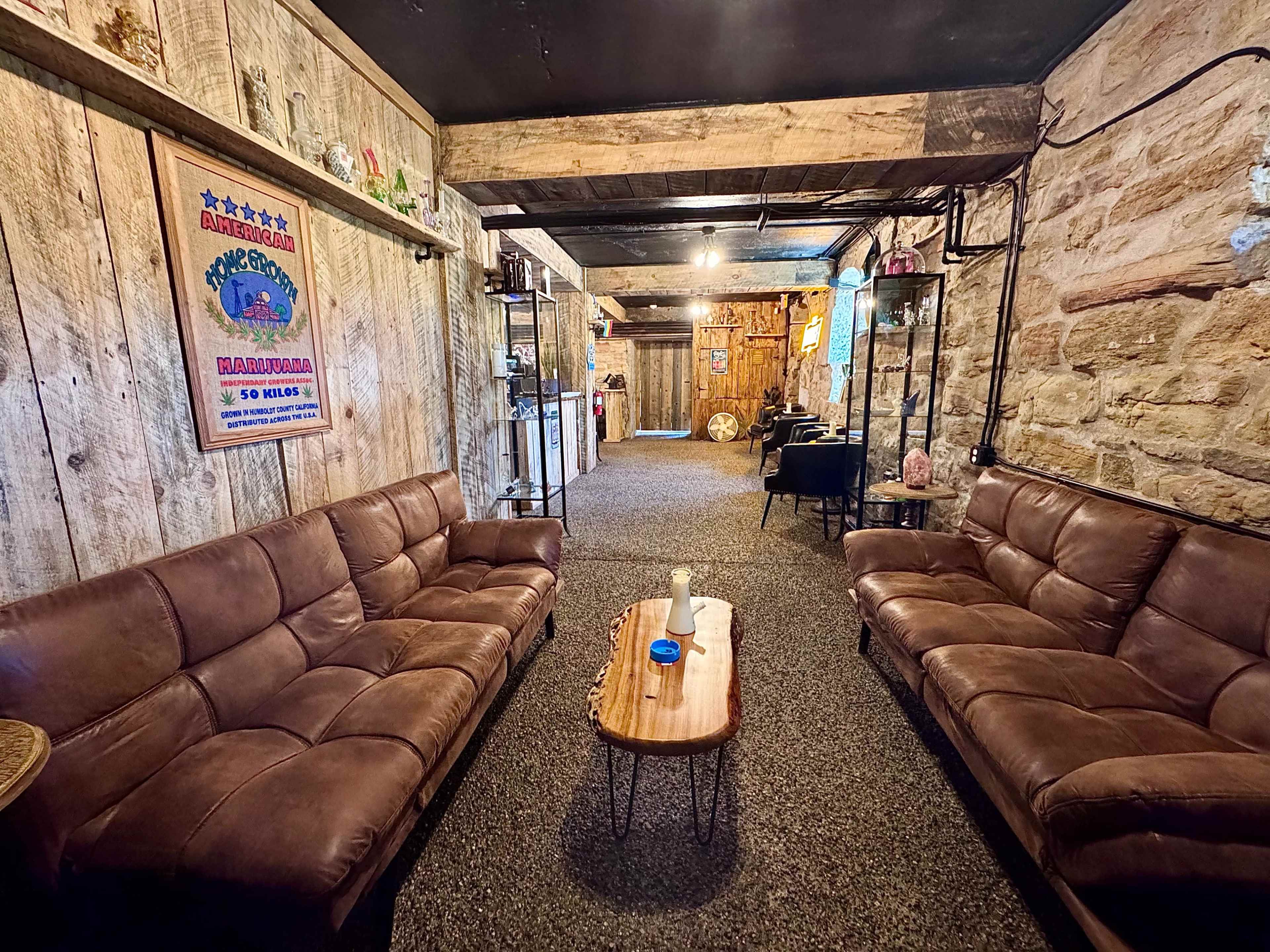 The image shows a cozy interior space with leather sofas, a wooden coffee table, exposed stone walls, and rustic decor, illuminated by soft lighting.