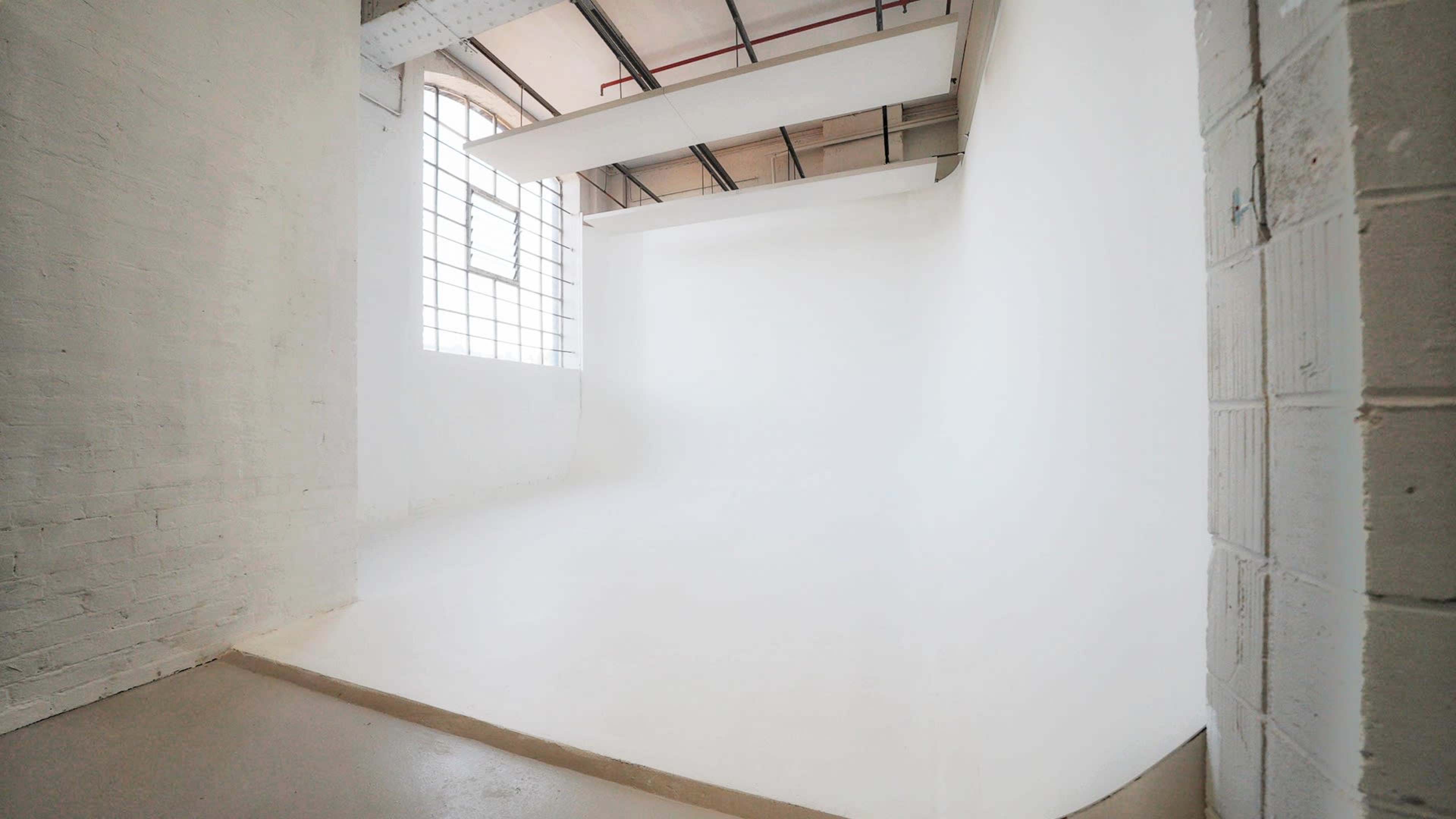 The image shows a minimalist studio space with a large window and a smooth, white wall extending into a seamless curved floor.