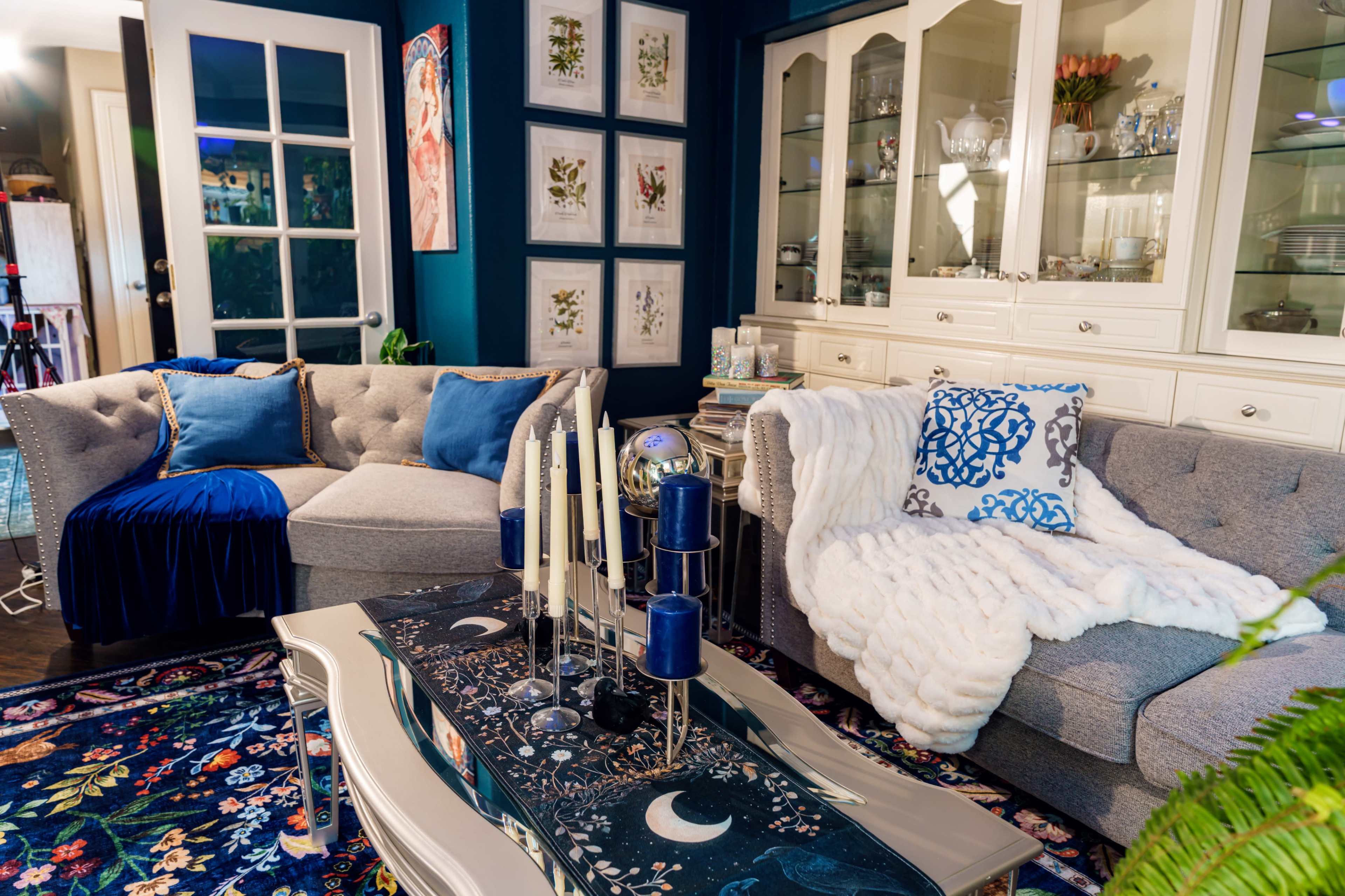 The image shows a stylish living room featuring two sofas, decorative pillows, a coffee table adorned with candles and decor, and framed artwork on the walls.