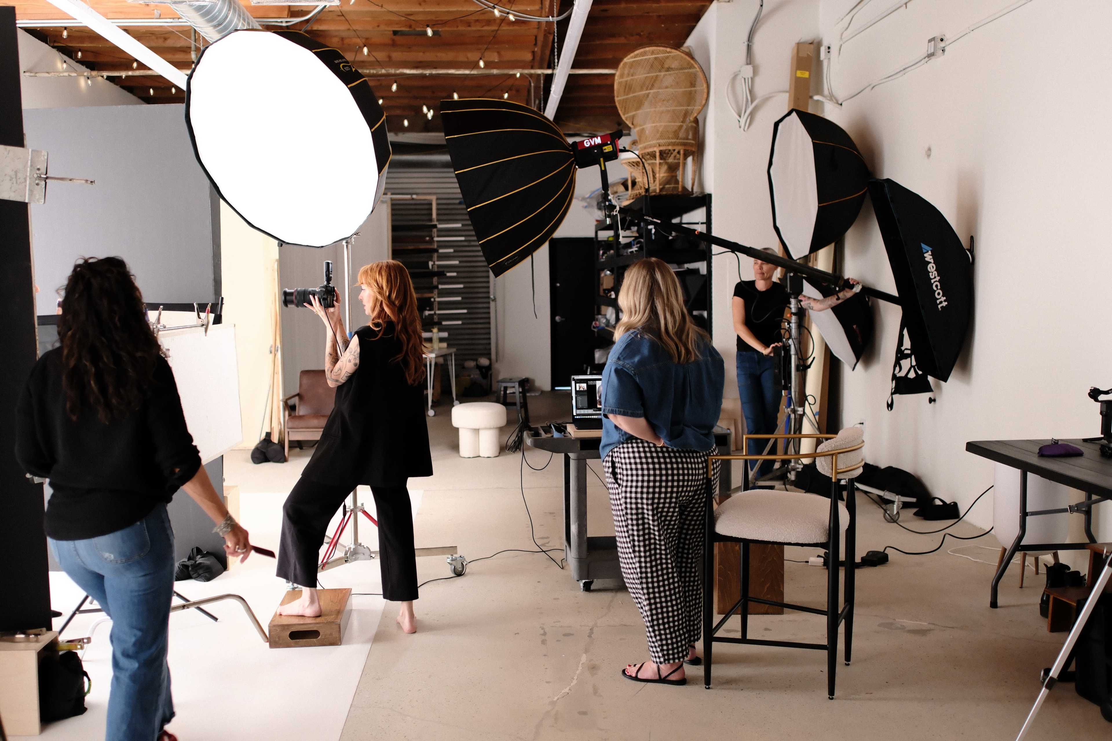 A group of photographers and models work in a well-lit studio equipped with multiple light sources and backdrops.