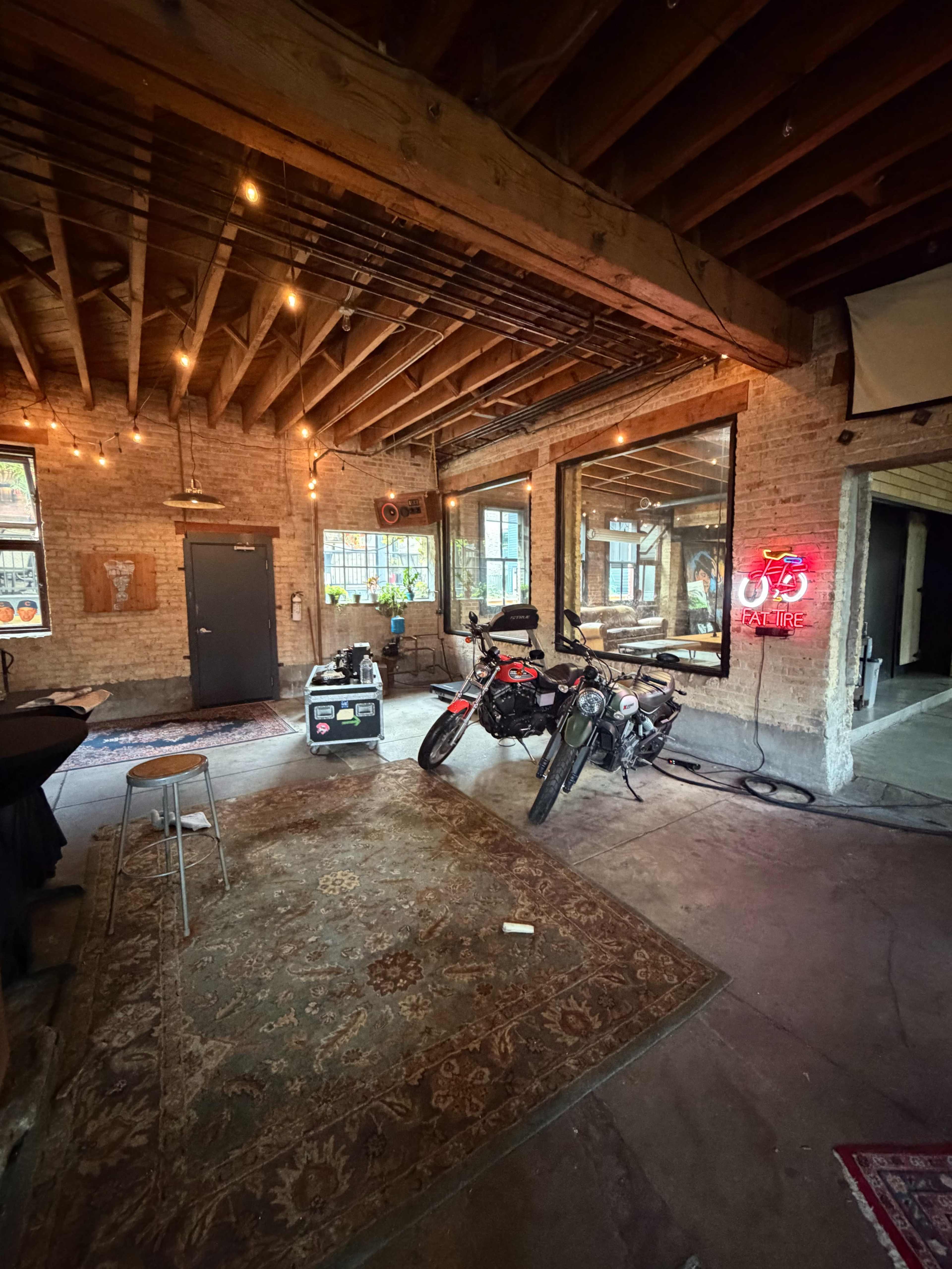 The image shows an industrial-style loft with exposed brick walls, wooden beams, and two motorcycles parked on a concrete floor.