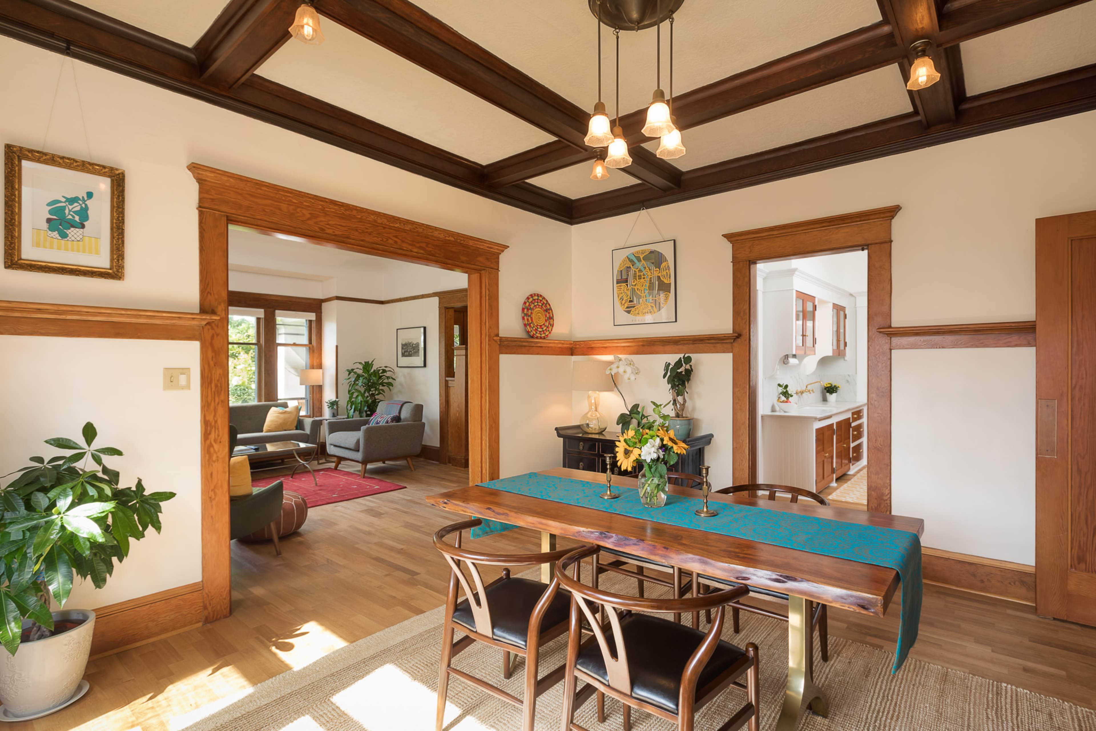 A dining area with a wooden table and chairs is connected to a living room, featuring large windows and an open layout.