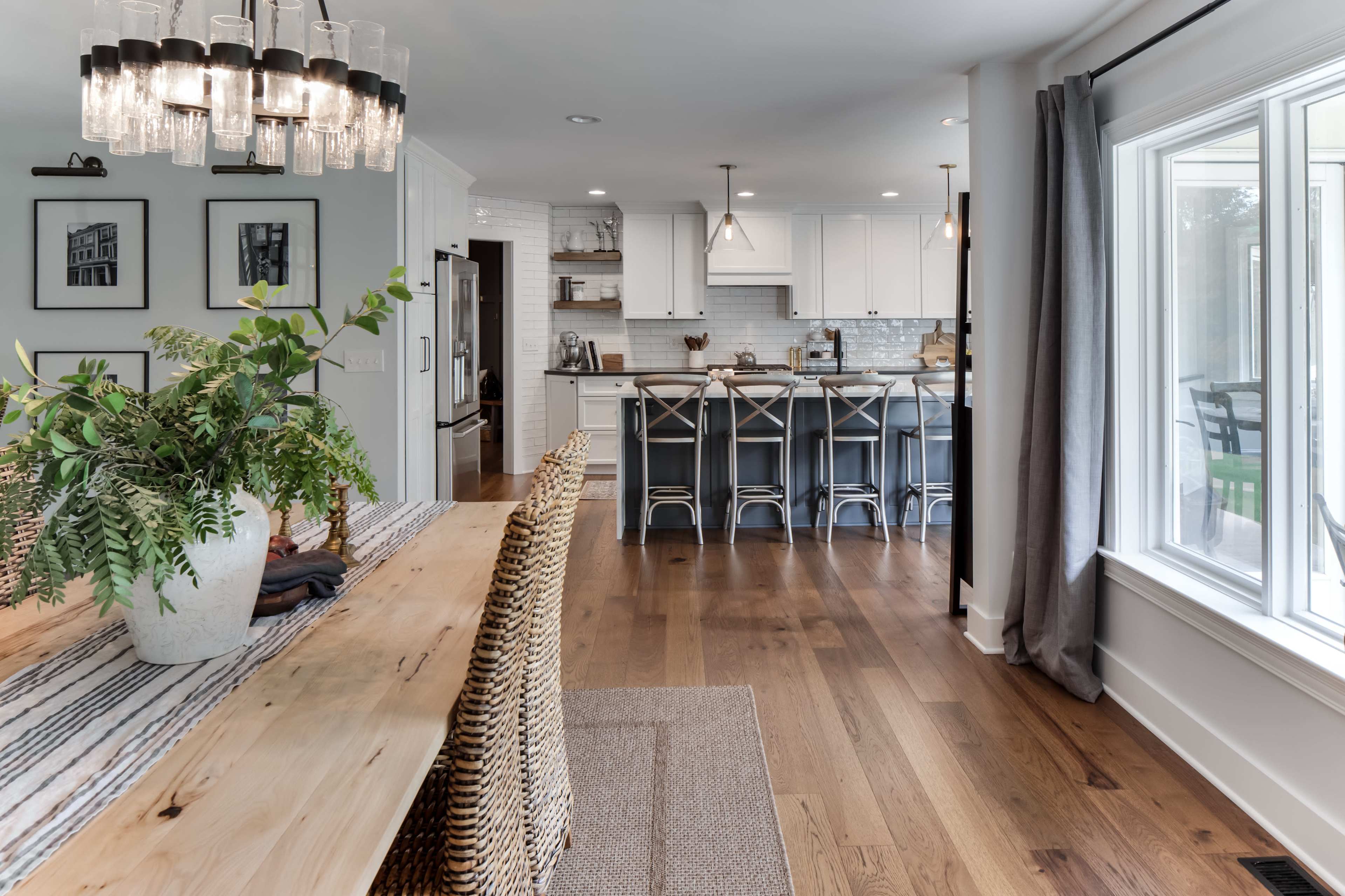 A modern kitchen and dining area with a wooden dining table, wicker chairs, and a kitchen island with bar stools.