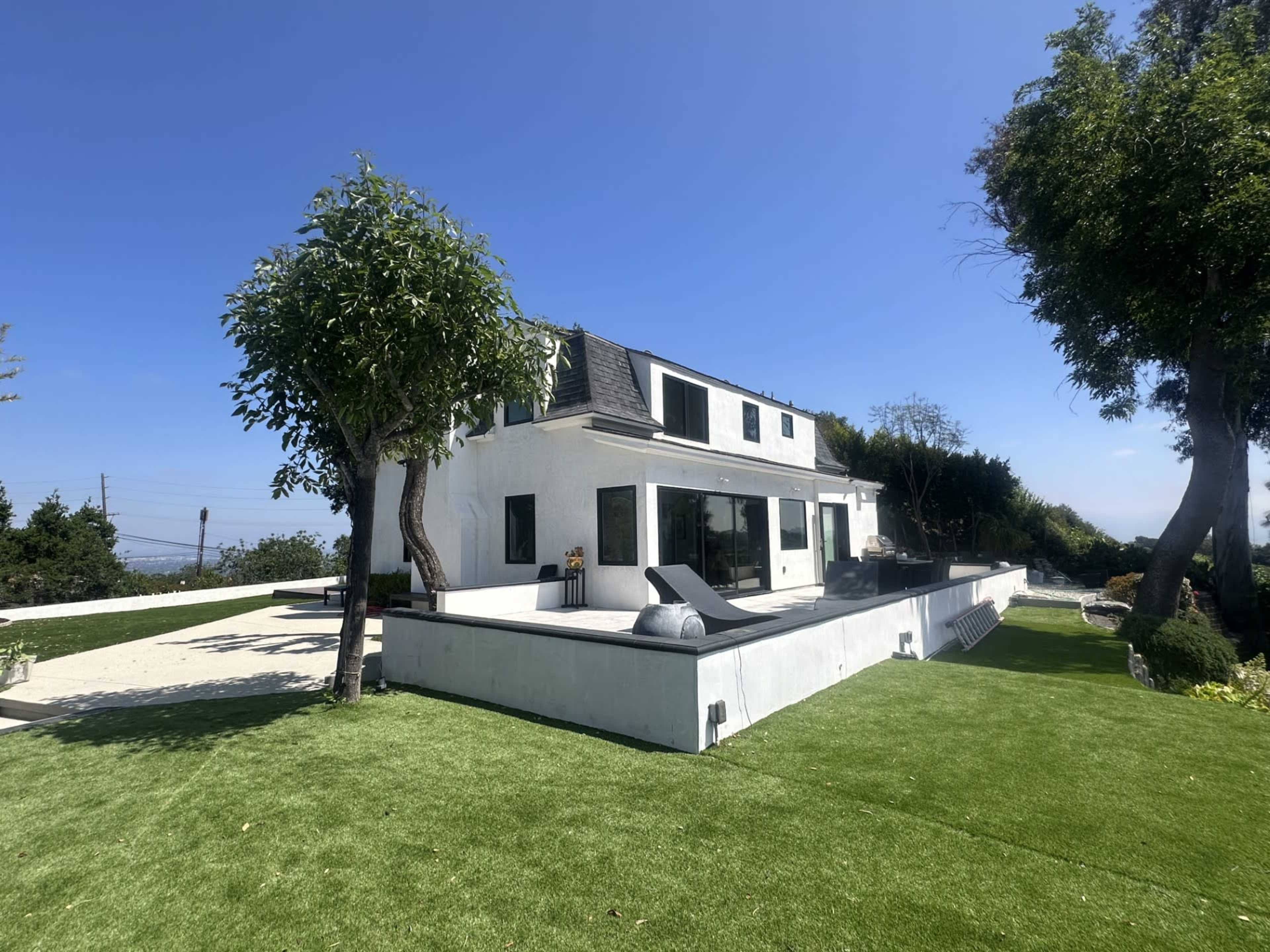 A modern two-story house with a white exterior and a landscaped yard featuring artificial grass and trees.