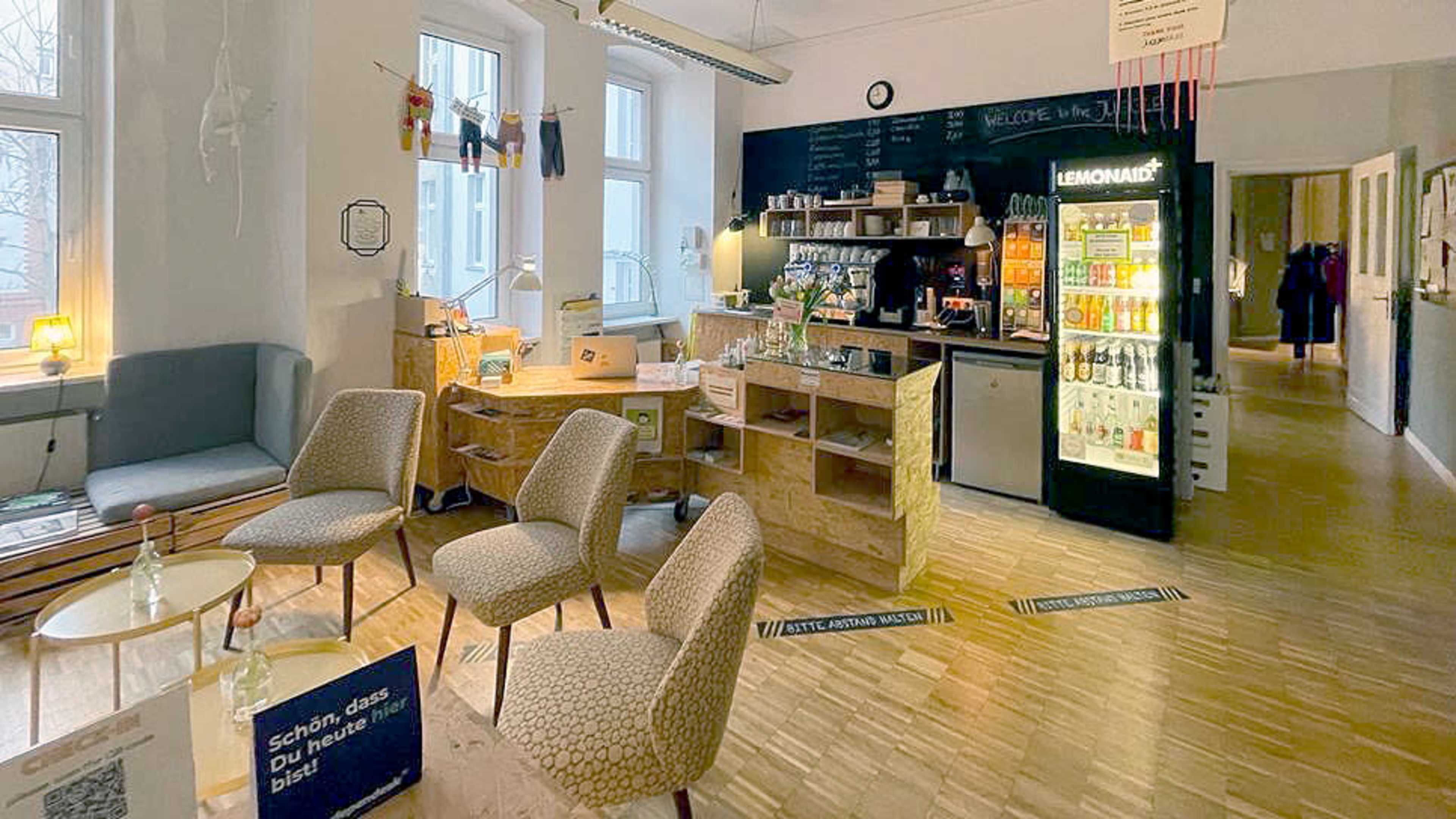 A cozy interior space featuring a café area with wooden furniture, shelves of beverages, and a seating area with chairs and tables.