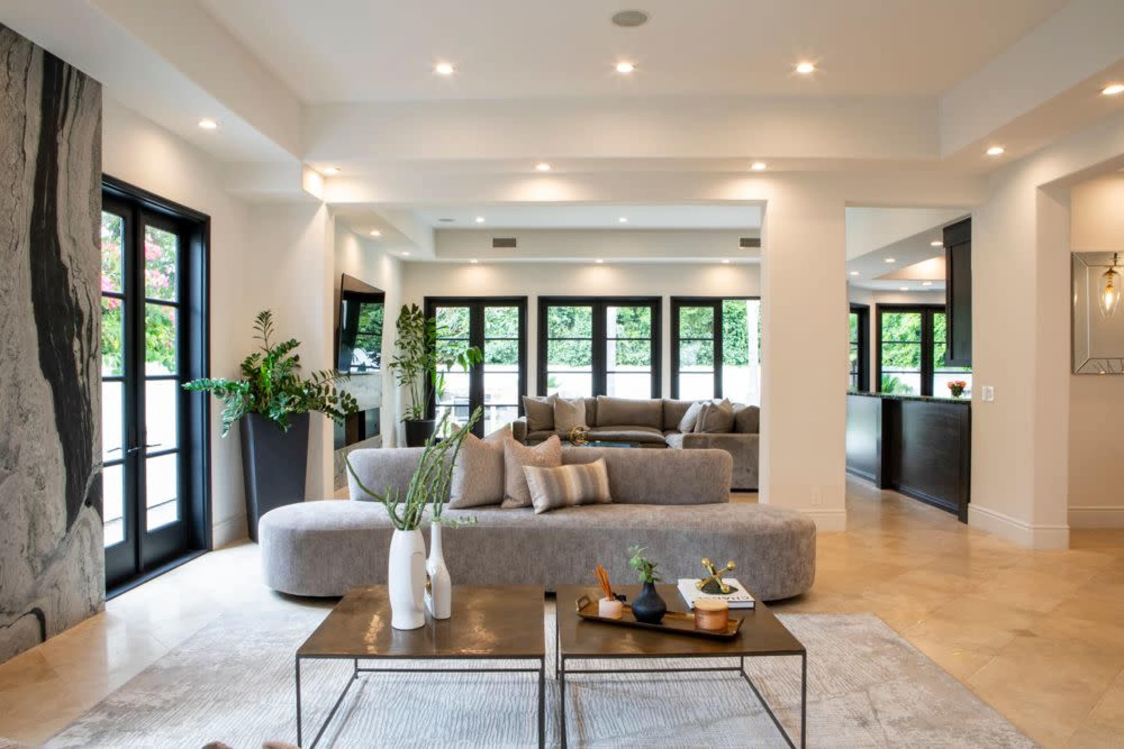 A spacious living room features sleek gray furniture, large windows, and modern decor elements.