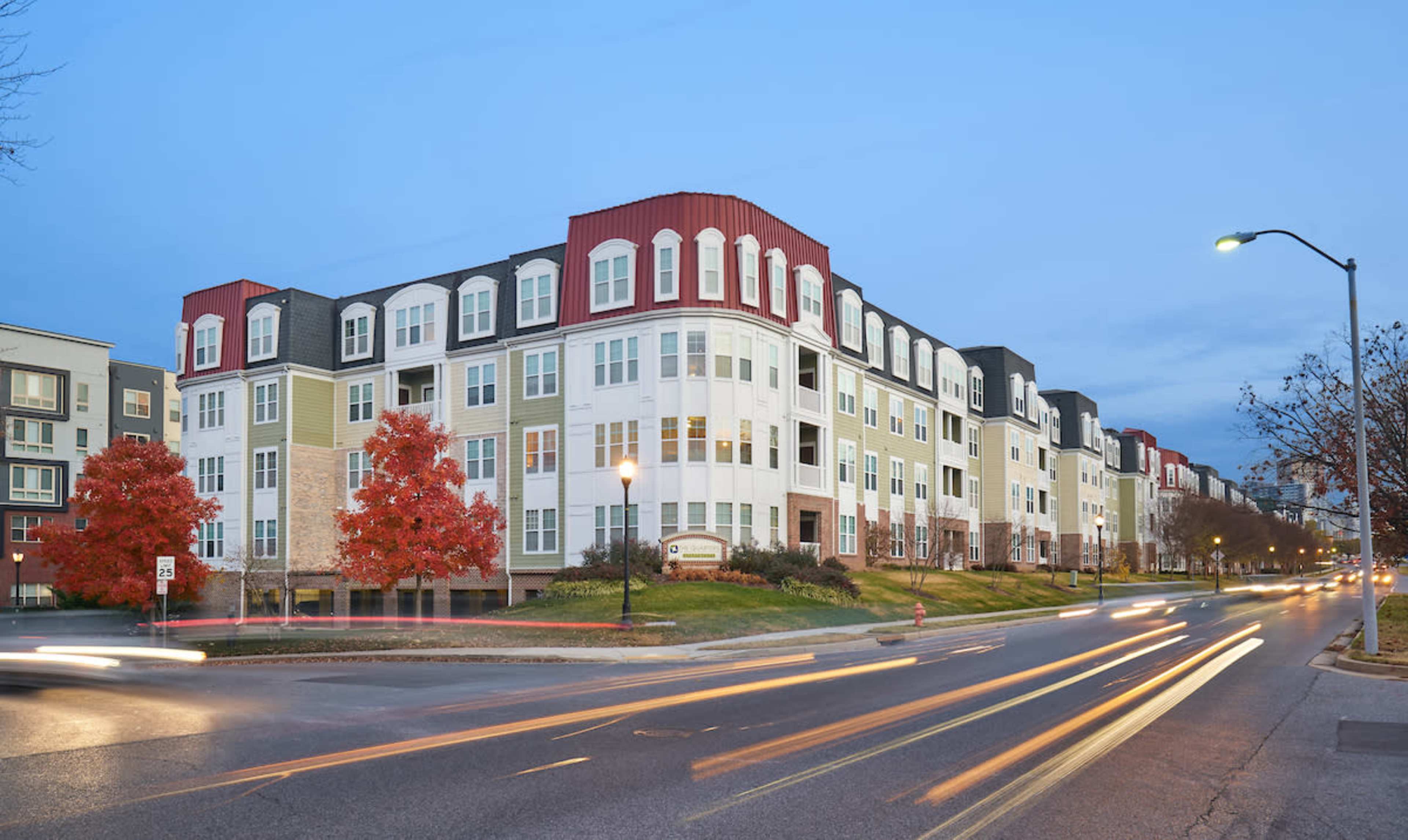 A multi-story residential building with a distinctive roof design, located along a tree-lined street, illuminated by streetlights.