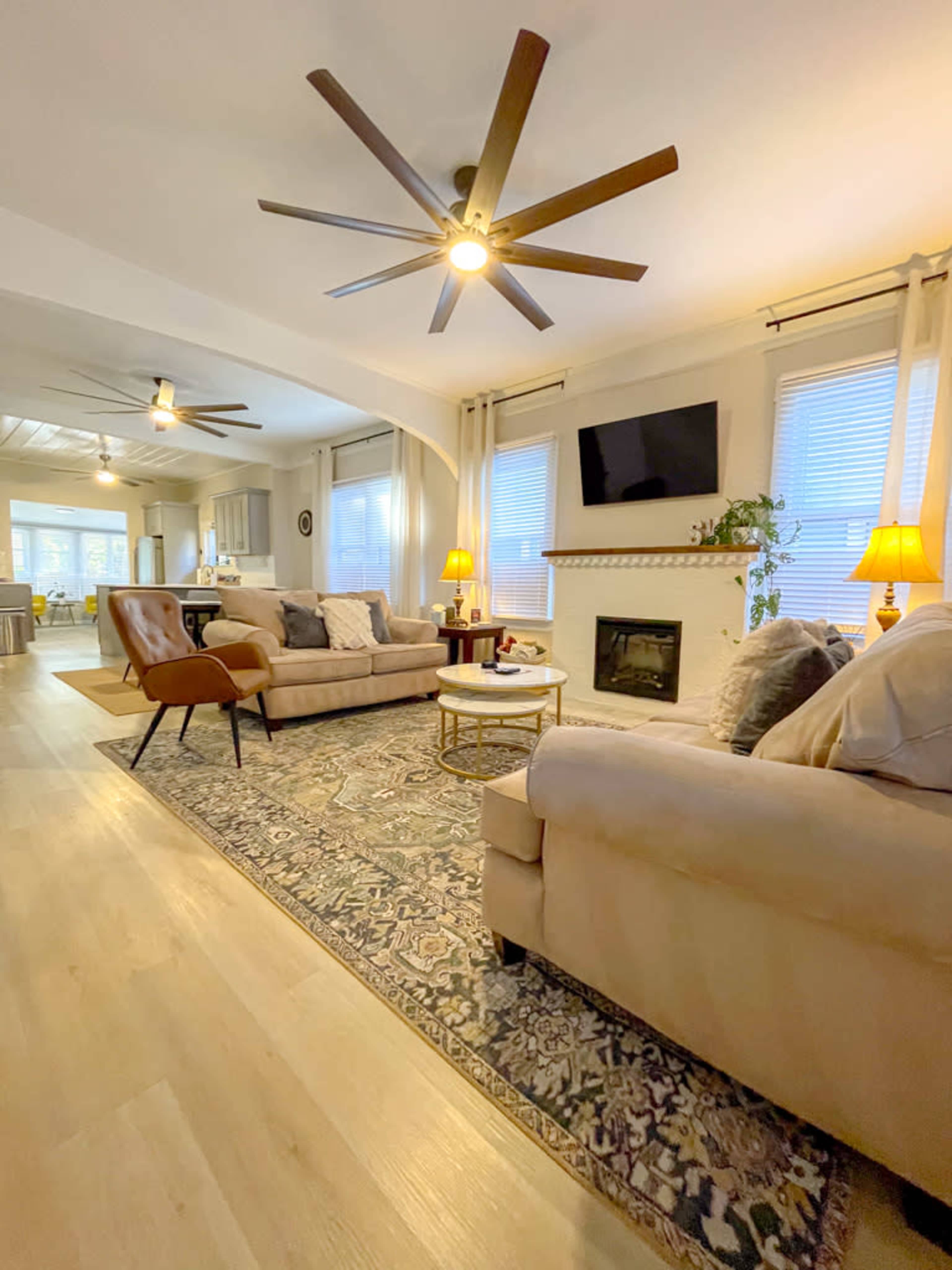 The living room features two sofas, a coffee table, and a fireplace, with large windows allowing natural light to fill the space.