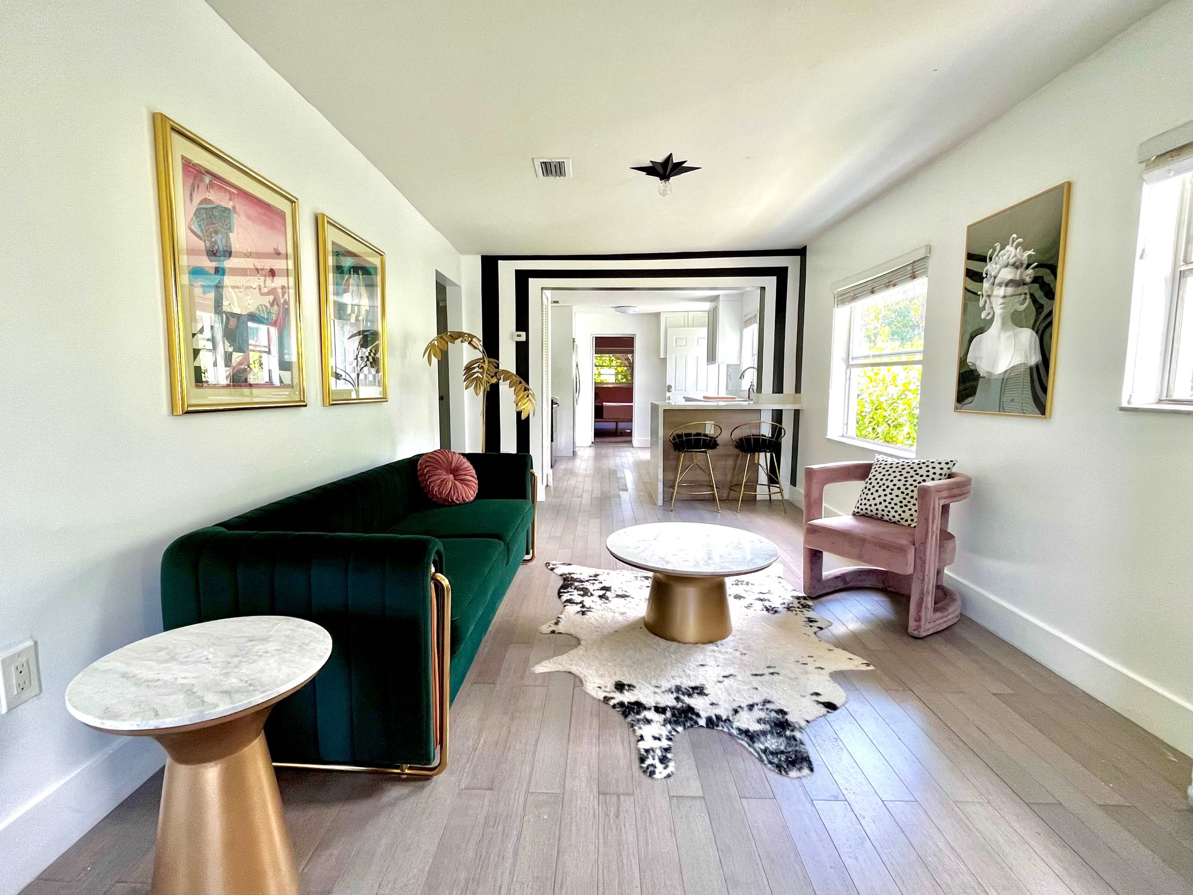 A modern living room with a green velvet sofa, a marble-top coffee table, and a pink chair, all set against a backdrop of framed artwork and minimalistic decor.