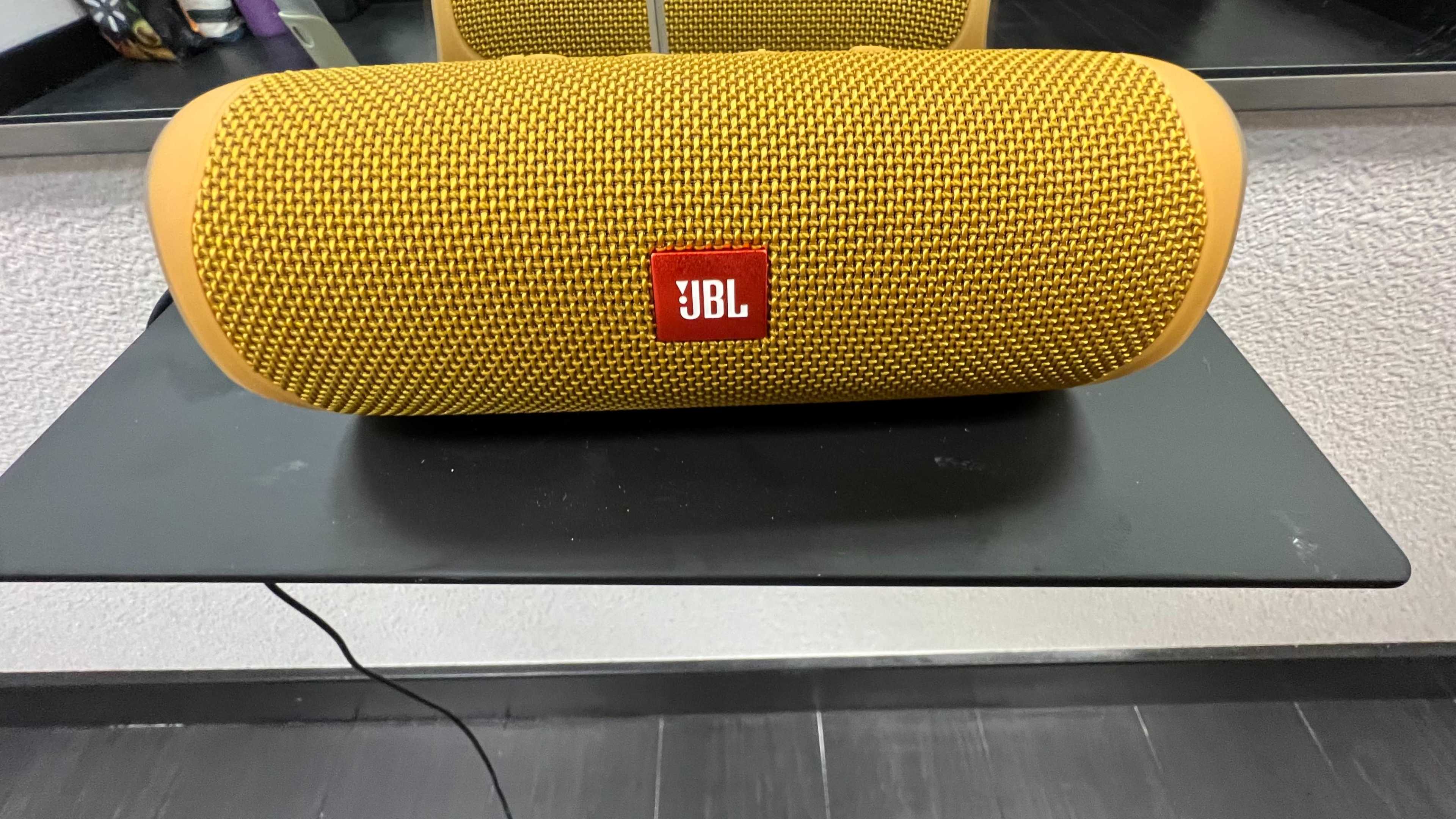 A yellow JBL portable speaker sits on a black table in front of a mirror.
