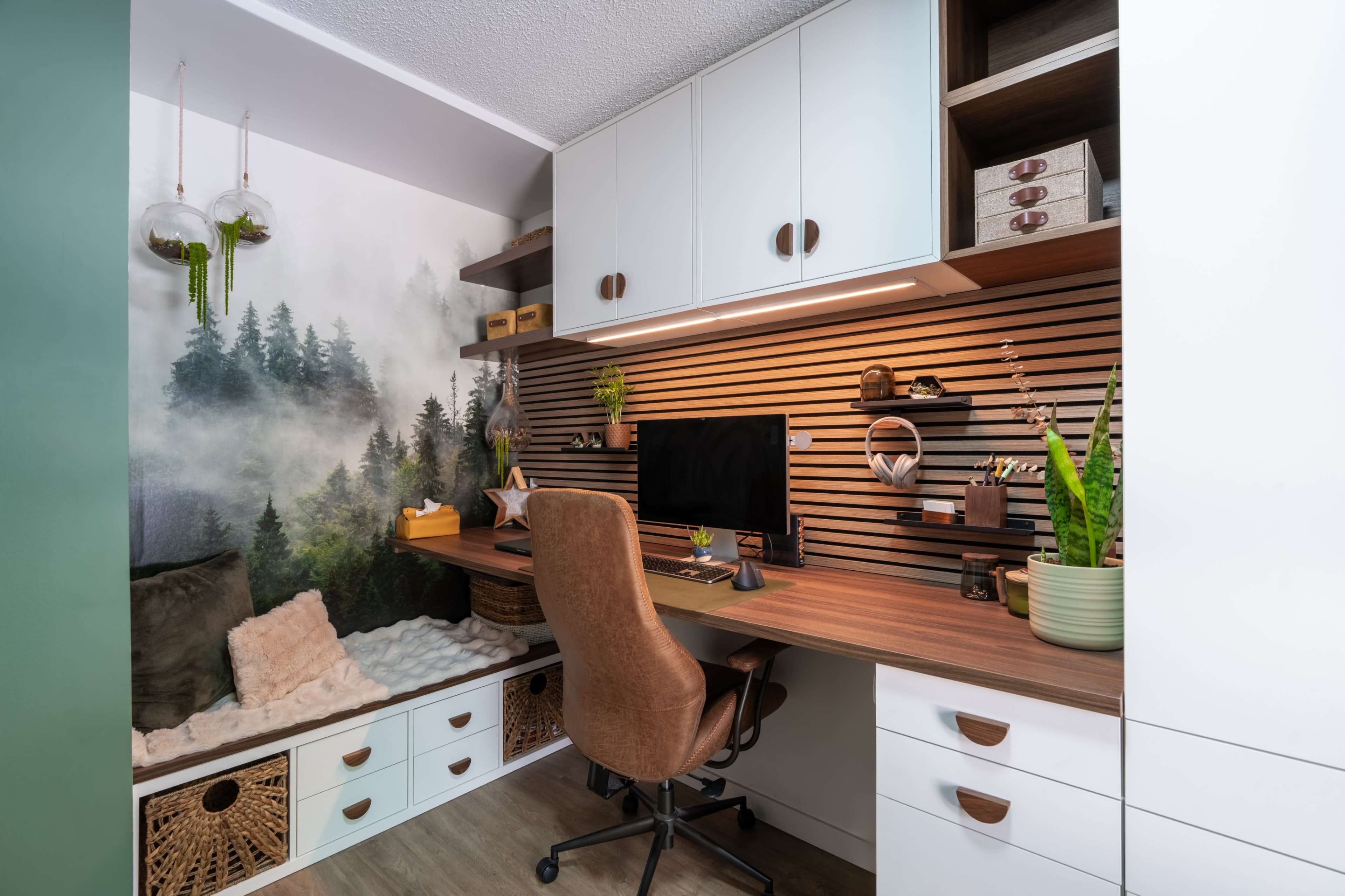 A modern home office features a wooden desk, an office chair, and a wall decorated with a forest mural, with shelves displaying storage boxes and plants.