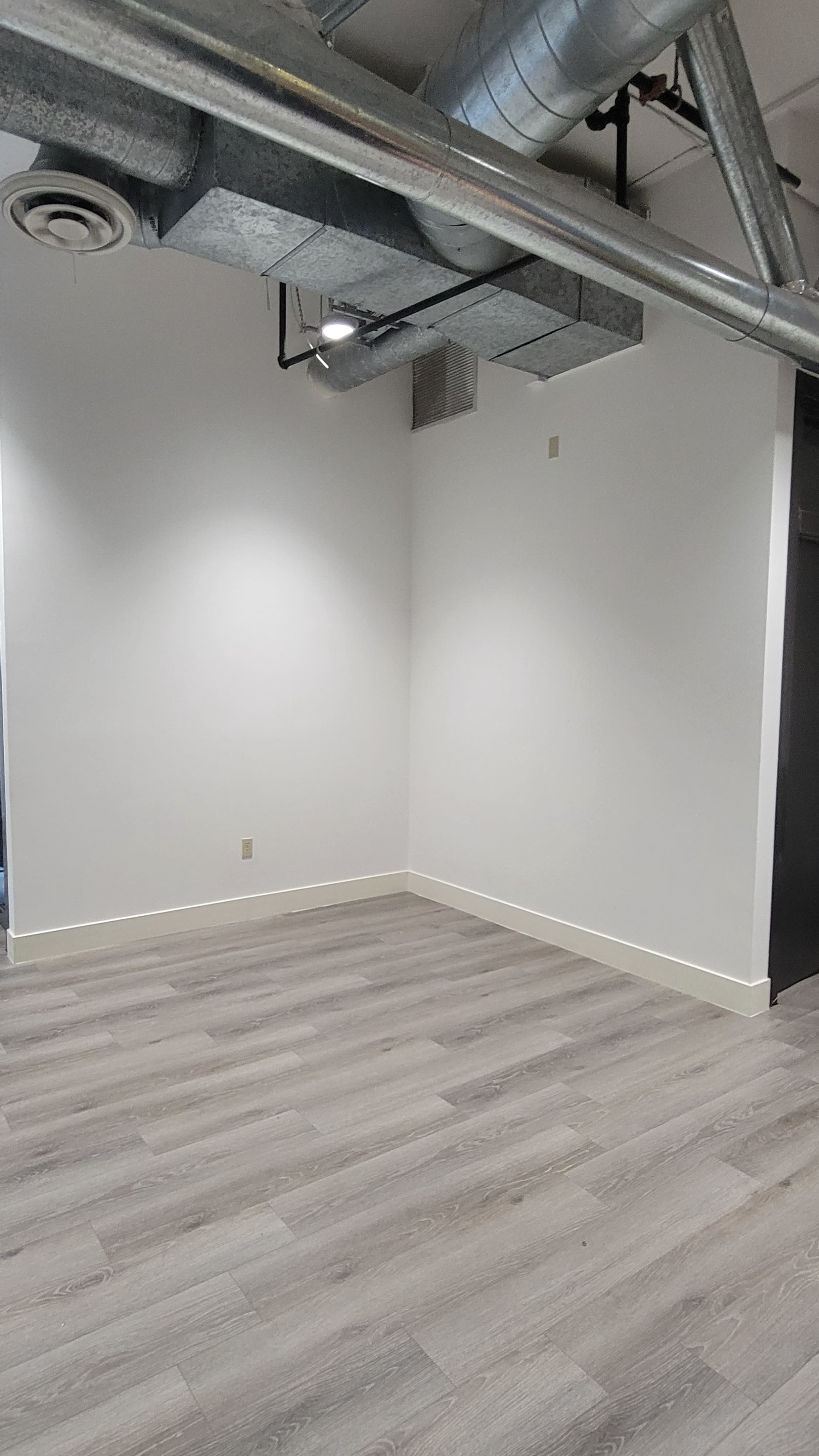 A vacant, minimalist room with light-colored wooden flooring and exposed ductwork on the ceiling.