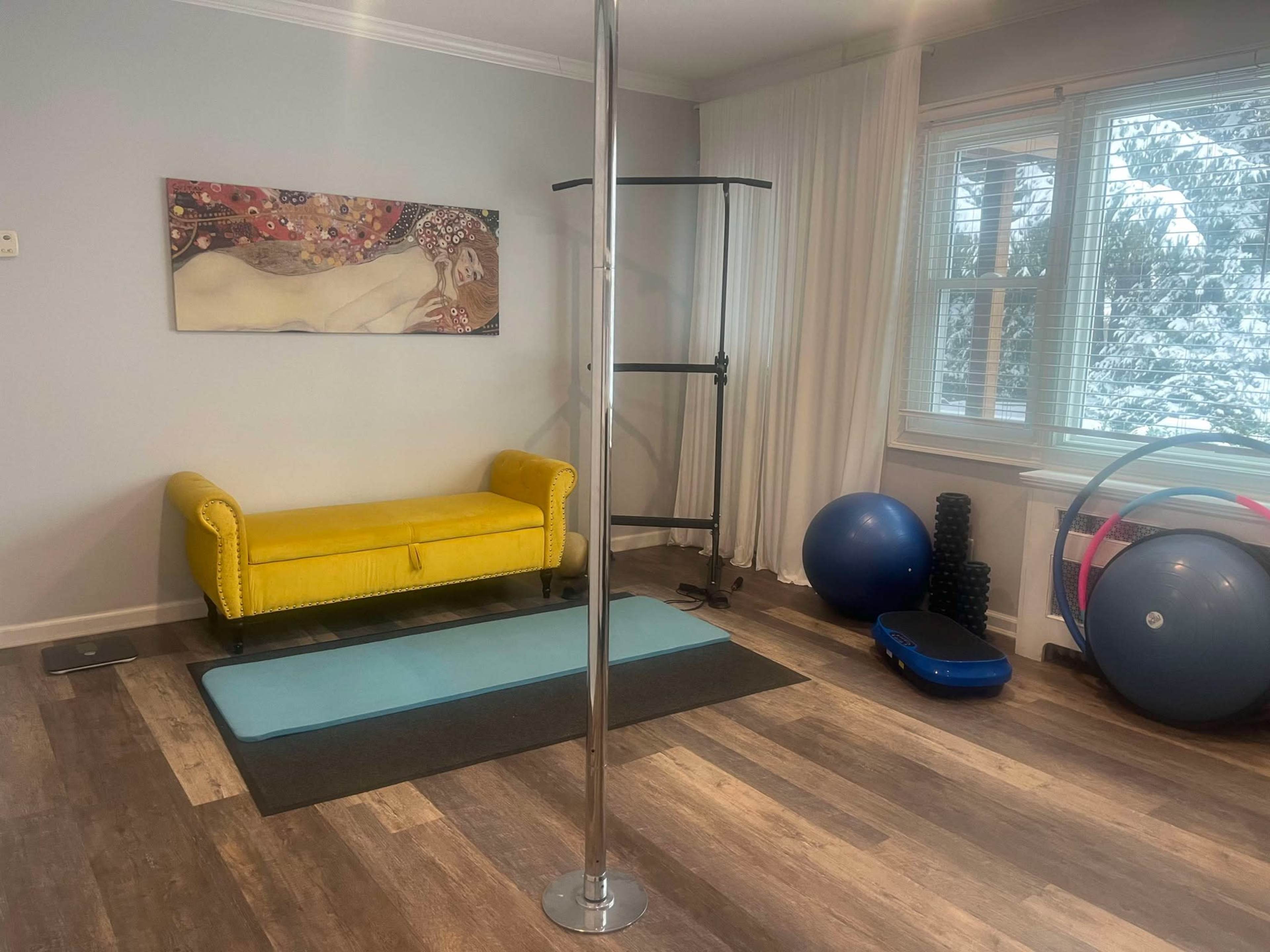 The image shows a home workout space featuring a yellow couch, a pole, exercise mats, and various fitness equipment.