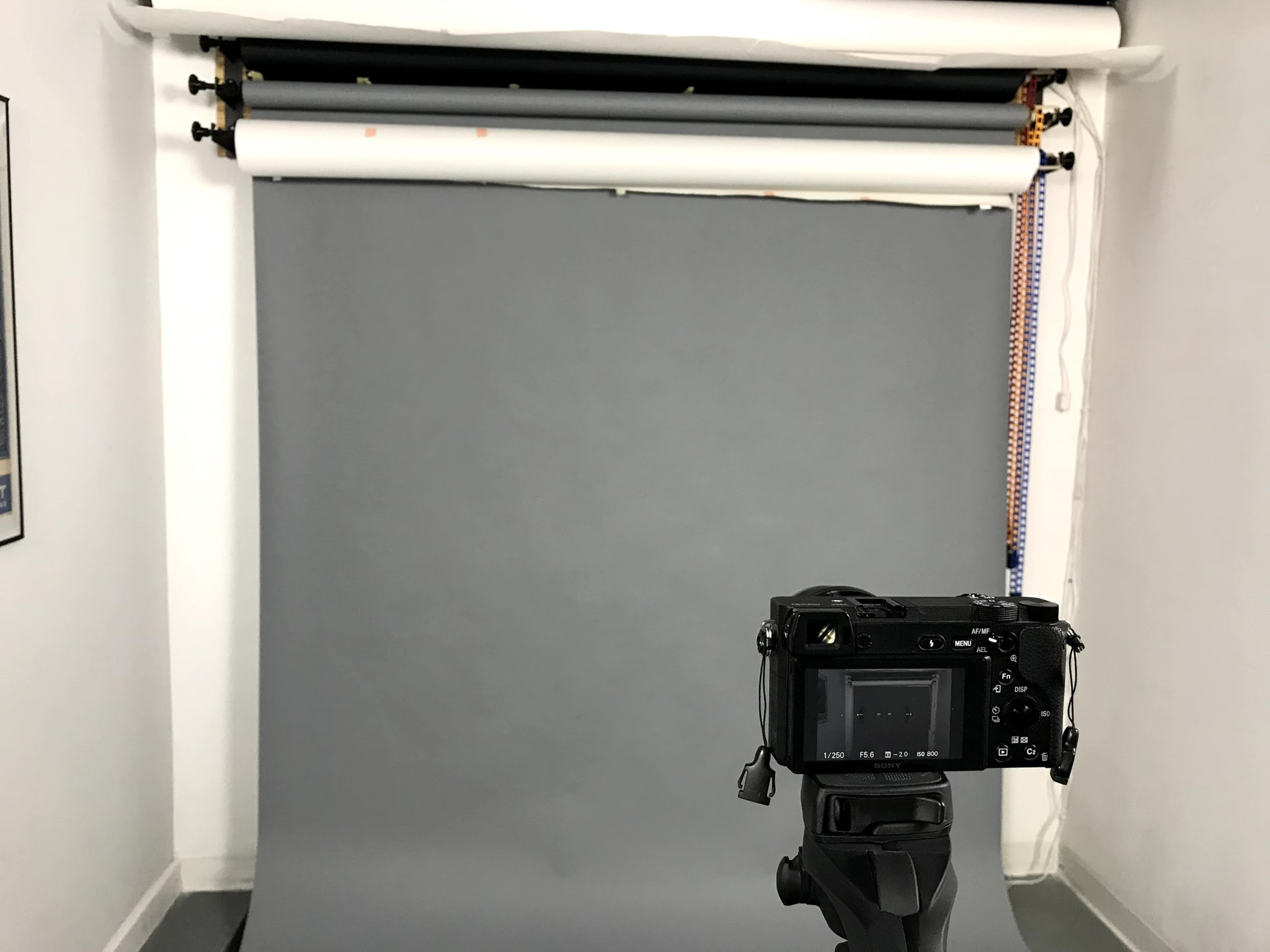 A camera on a tripod is positioned in front of a gray backdrop in a photography studio.