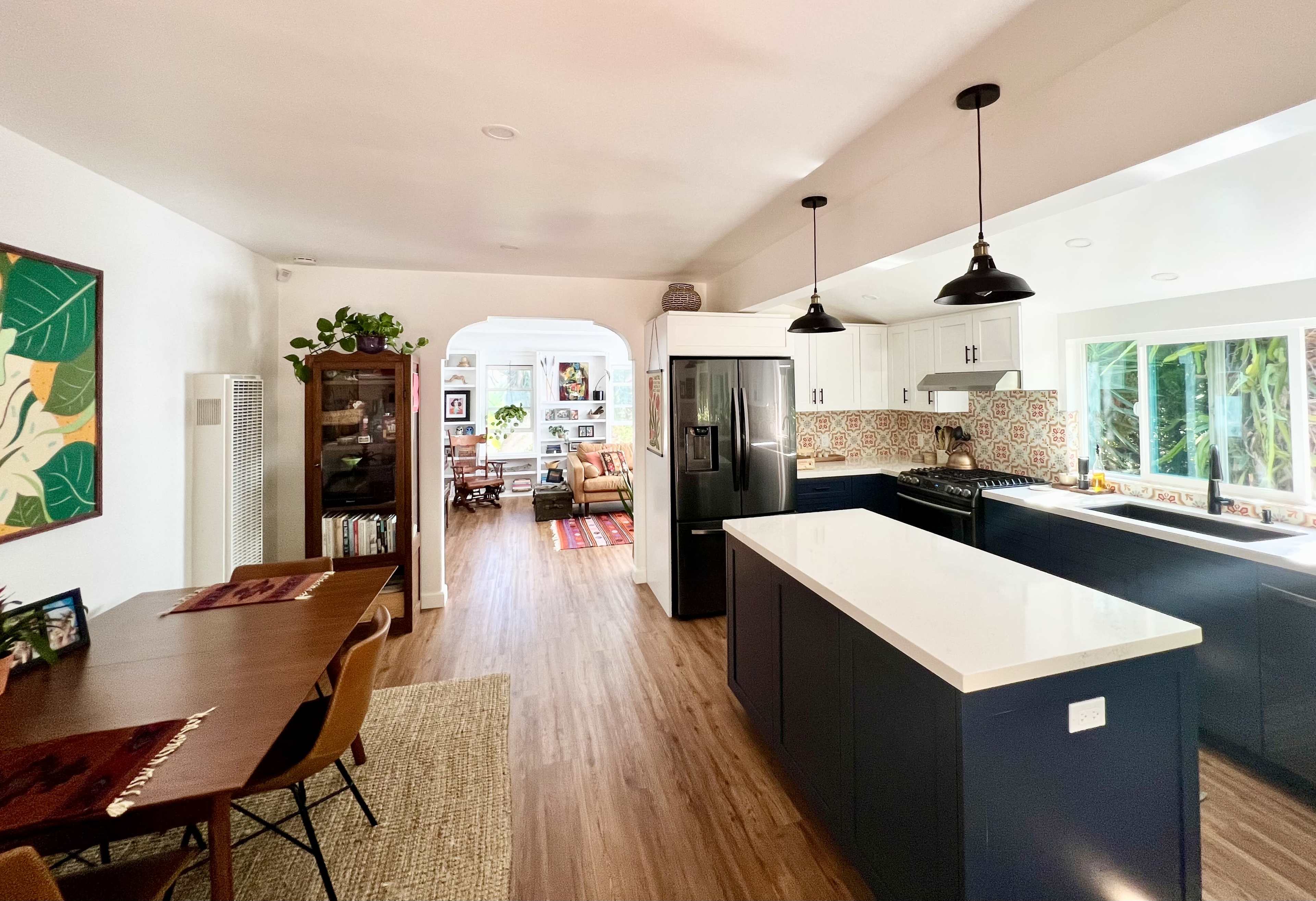A modern kitchen features dark cabinetry, a large island with a white countertop, and a view of a living space through an archway.