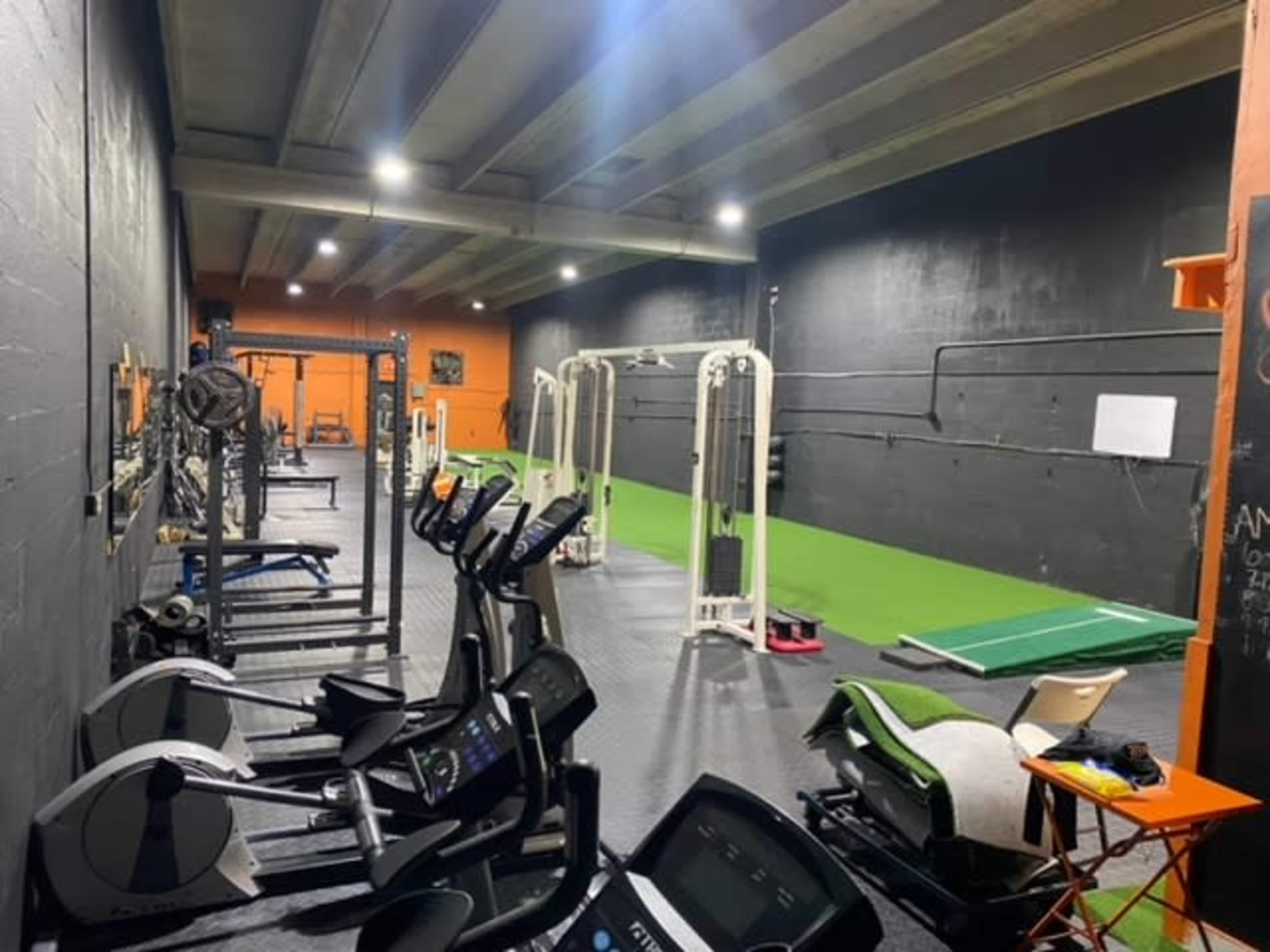A gym interior with various fitness equipment, including stationary bikes, a cable machine, and a green exercise area.
