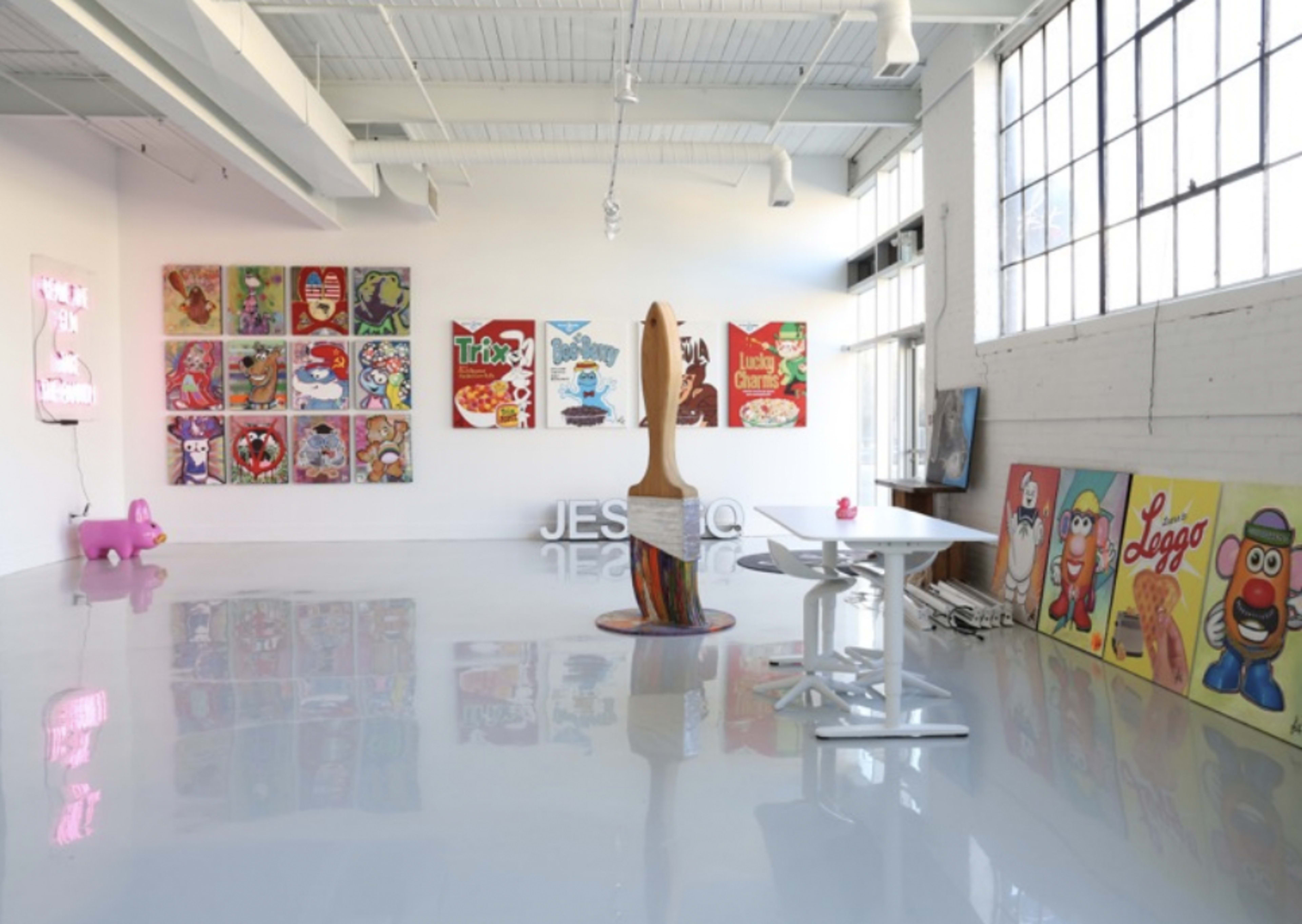 An art gallery featuring colorful collectible artwork on the walls and a central sculptural piece, with a clear floor and well-lit space.