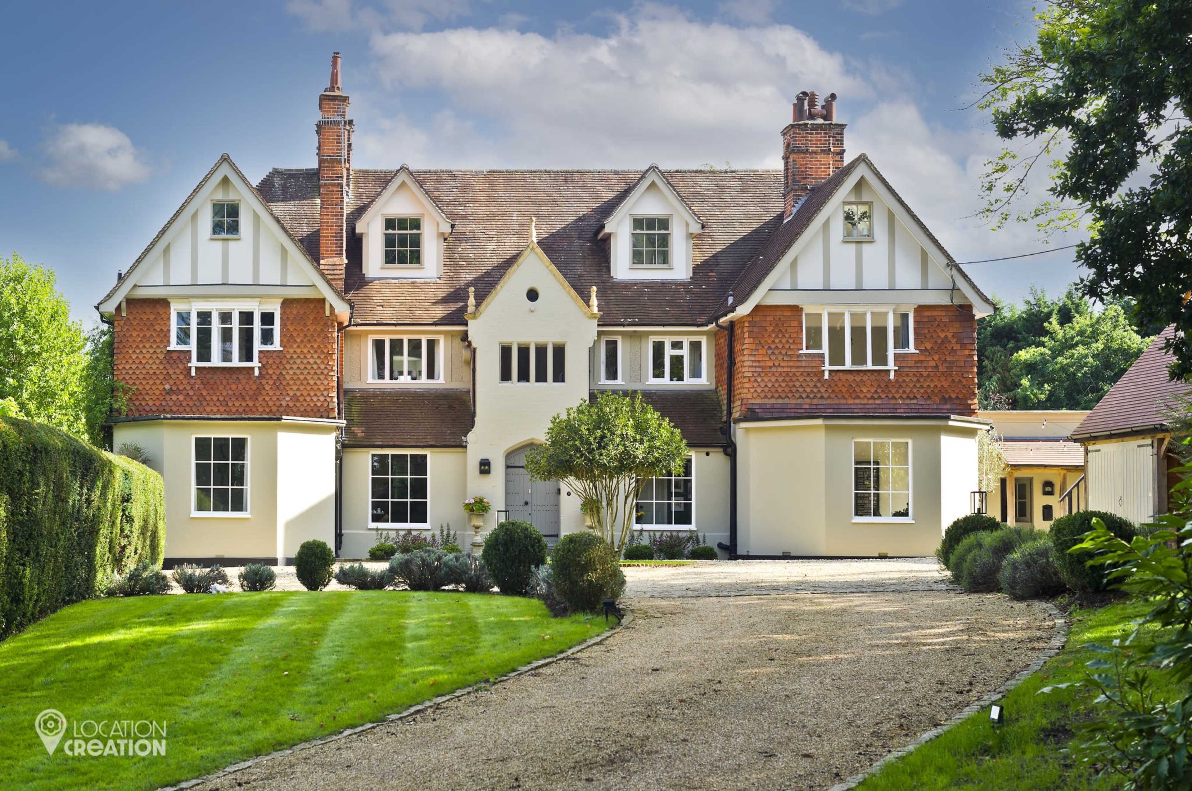 The image shows a large, two-story house with a mix of brick and stucco exterior, surrounded by a well-manicured lawn and gravel driveway.