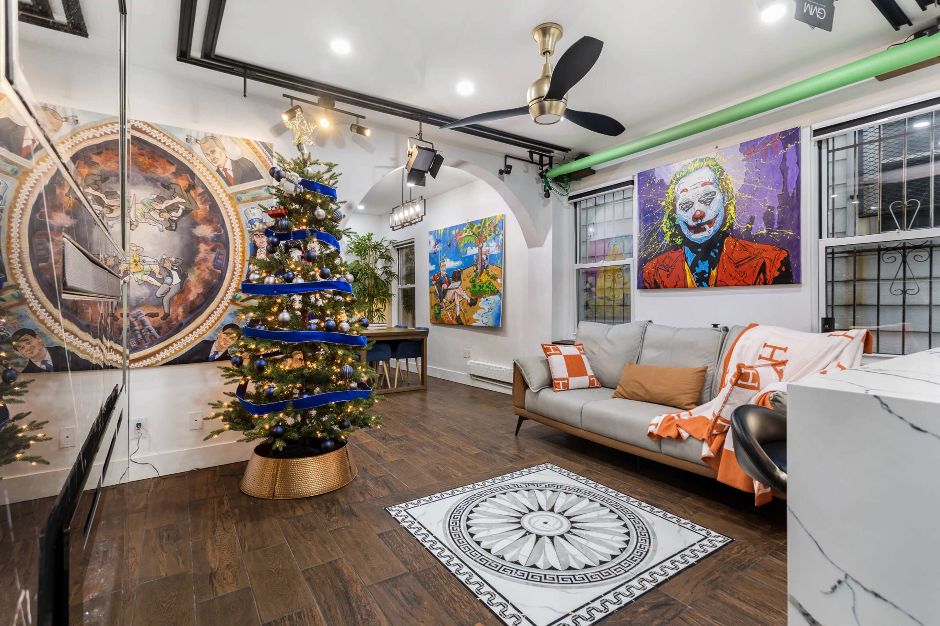 The image shows a modern living room decorated with a Christmas tree, contemporary artwork on the walls, and a light-colored sofa with an orange throw.