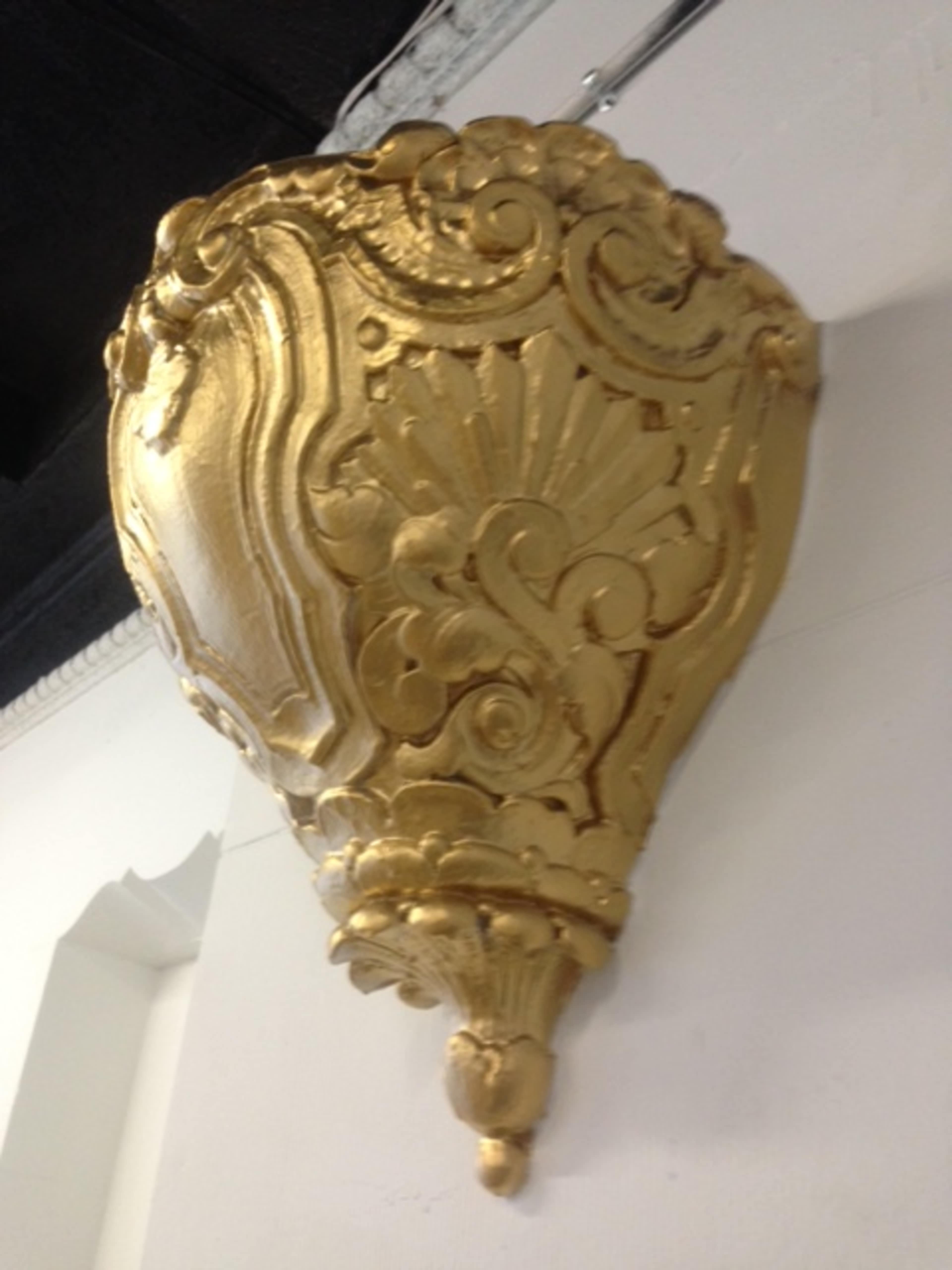 An ornate golden wall sconce with intricate designs hanging from a wall.