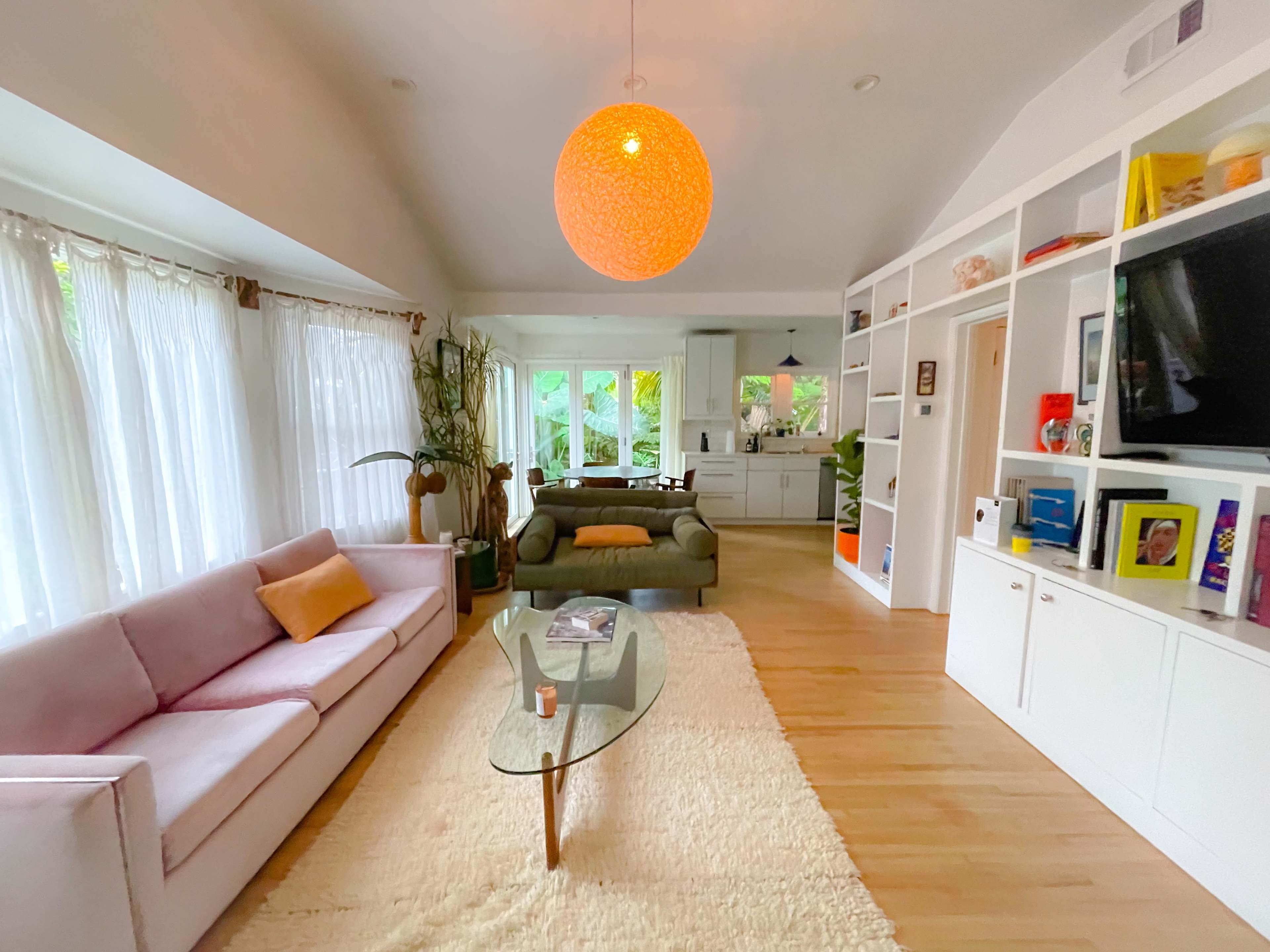 A modern living room with a light pink sofa, a green chair, a glass coffee table, and large windows allowing natural light.