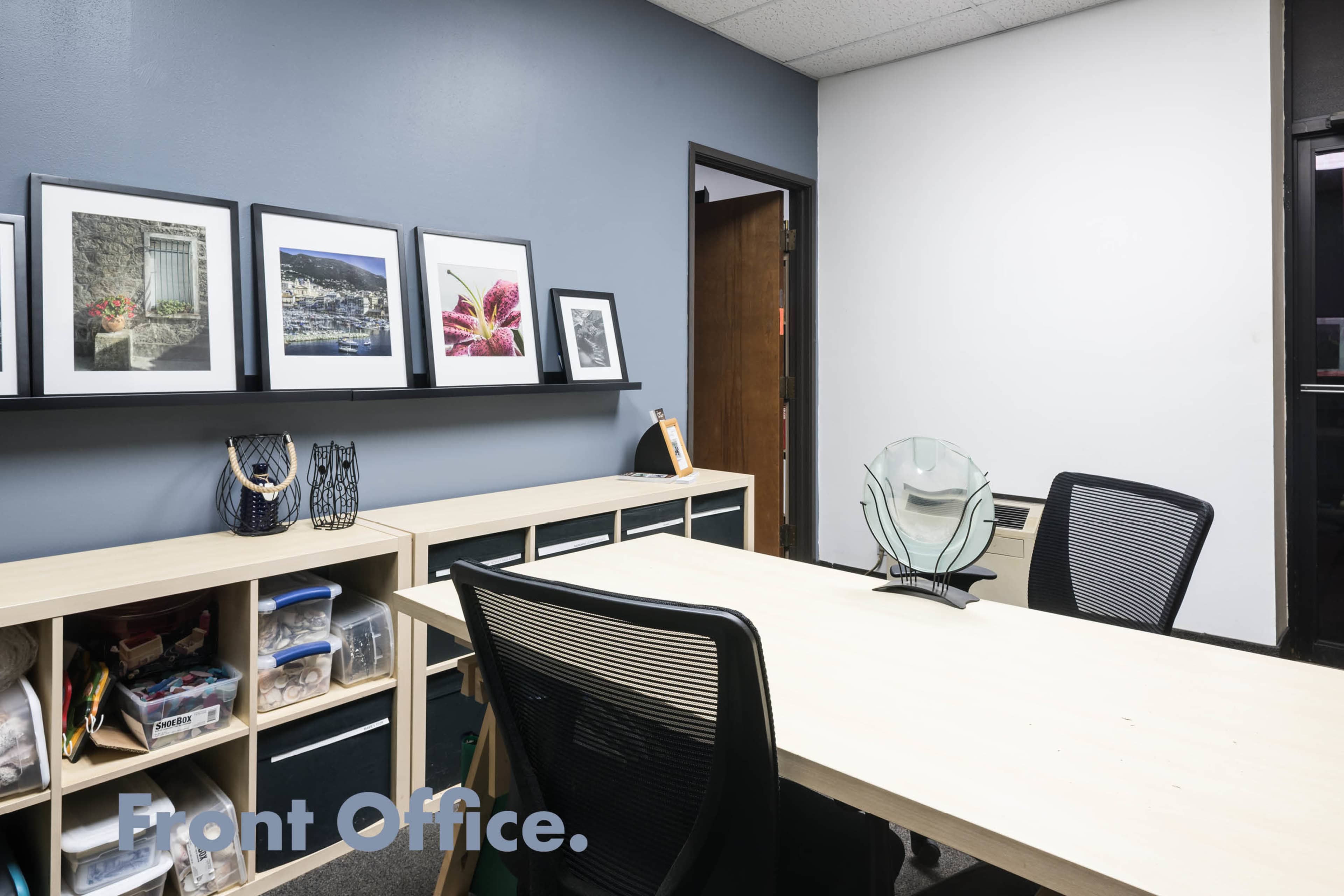 A front office space featuring a large table, framed artwork on the wall, and storage cubbies filled with various items.