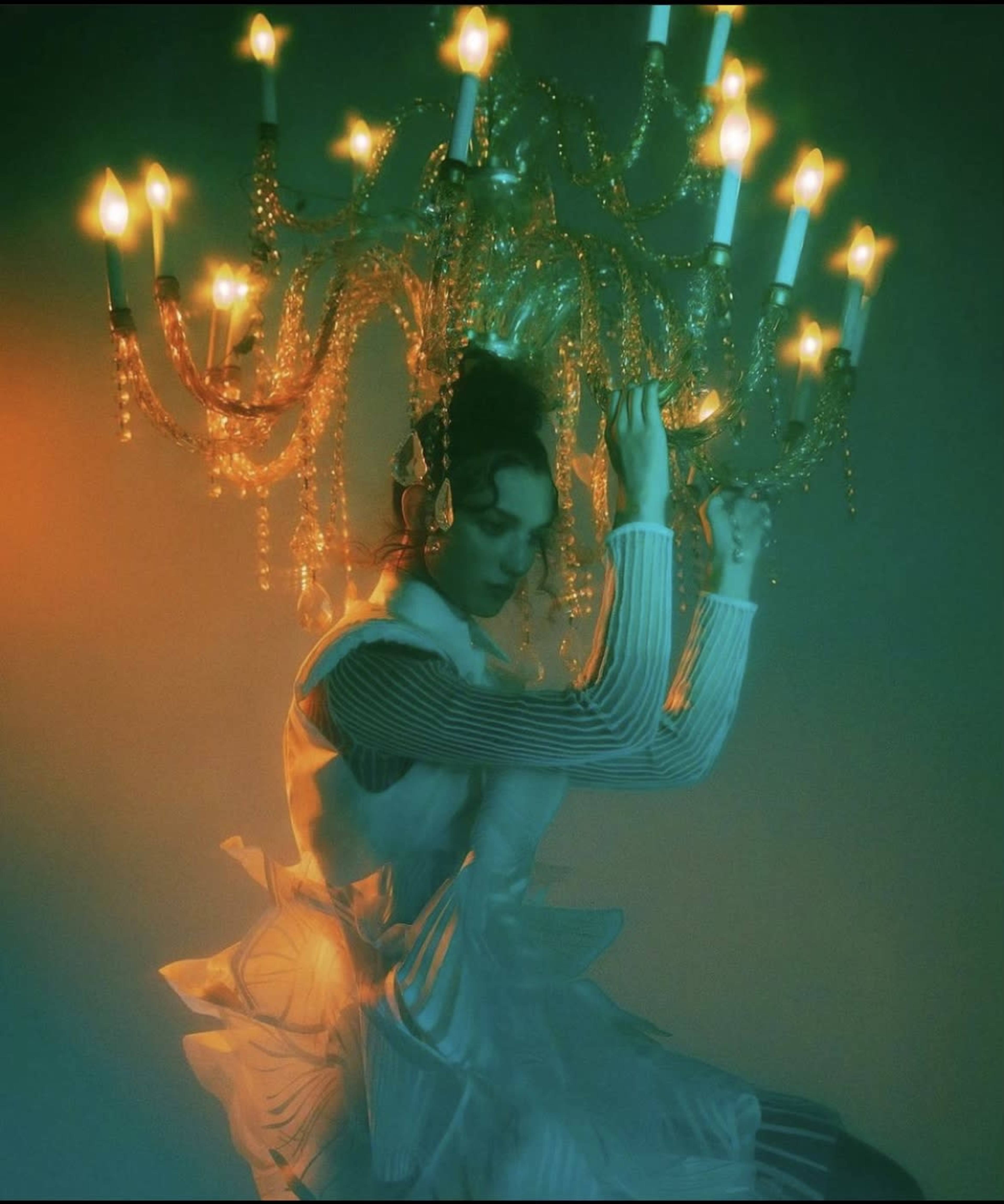 A woman in a white dress is holding a large, ornate chandelier surrounded by soft lighting.
