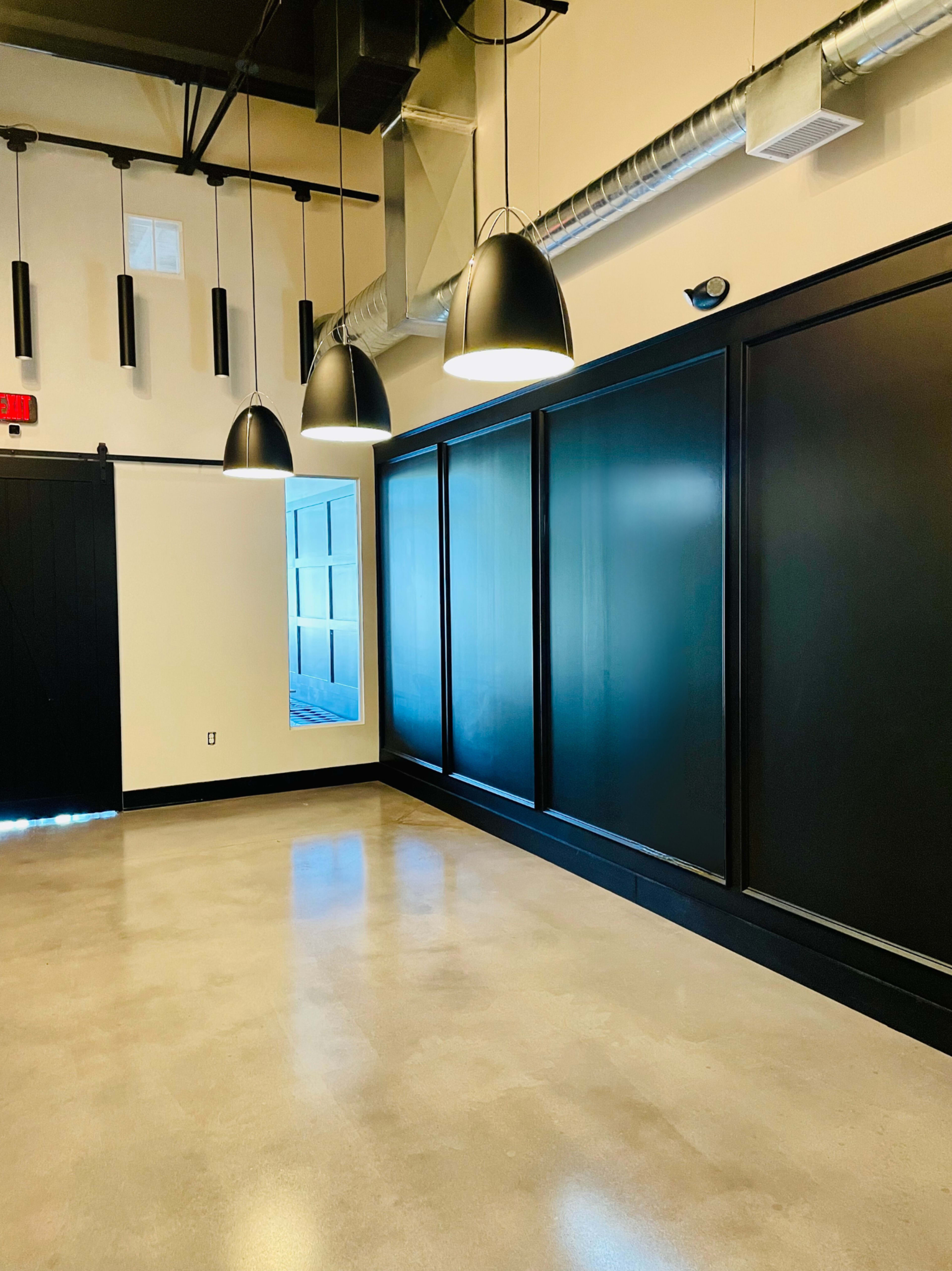 The image shows an indoor space with a polished concrete floor, black wall panels, and several pendant lights hanging from the ceiling.