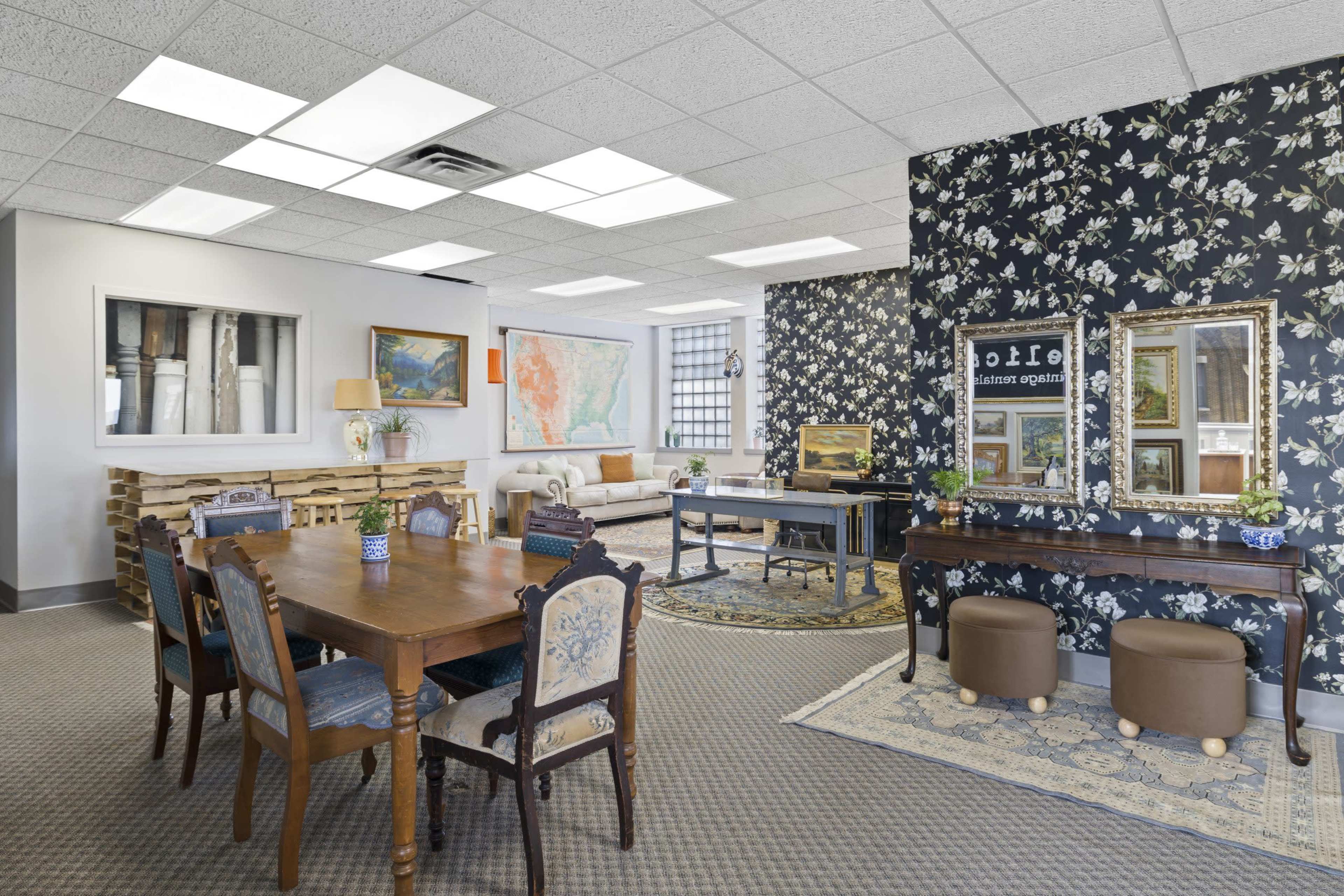 A bright office space with a dining table, chairs, and a patterned accent wall, featuring a mix of furniture and decorative elements.