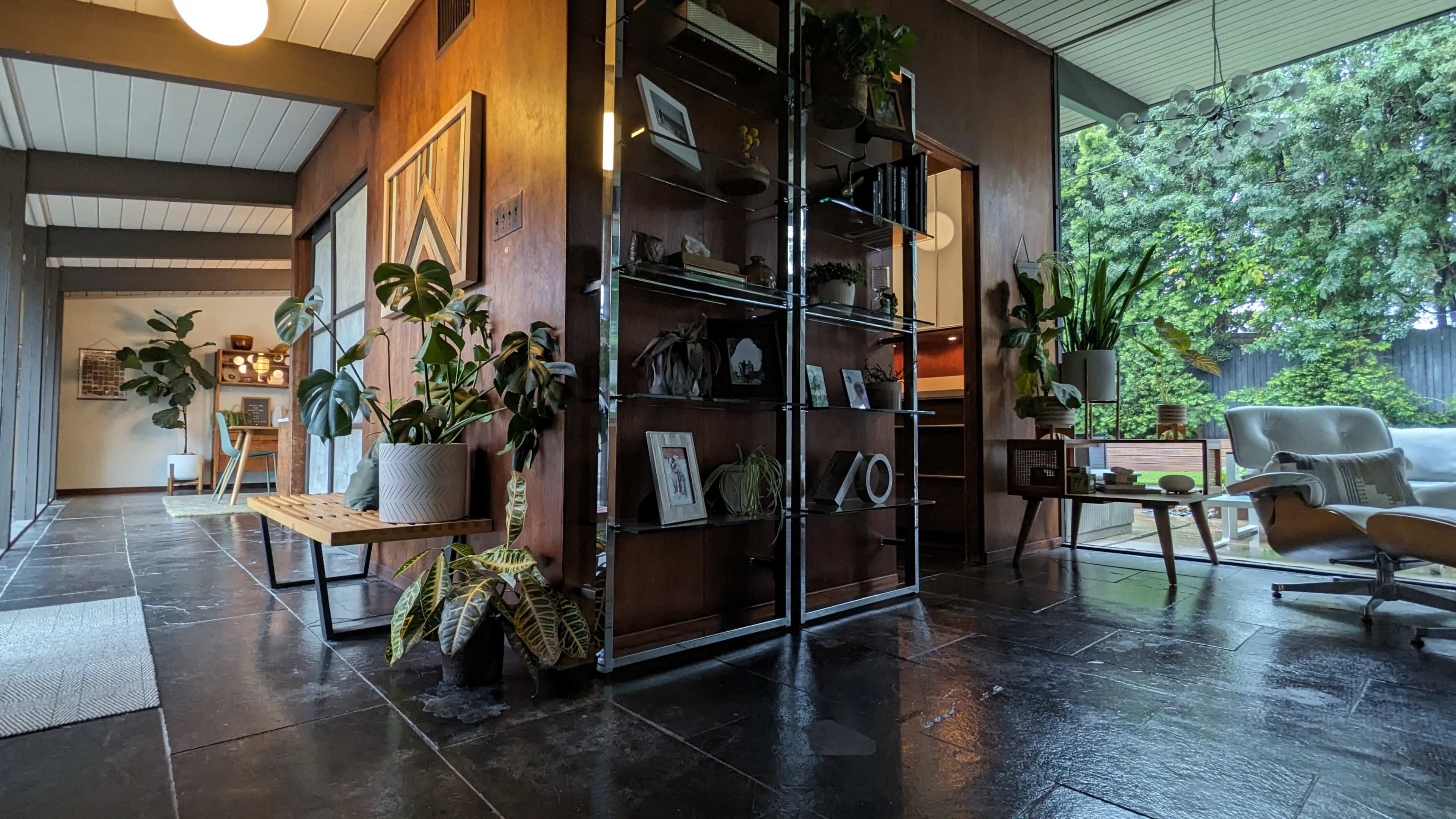 A modern interior space featuring a mix of plants, furniture, and decorative items arranged along a rectangular hallway with natural light streaming in from large windows.
