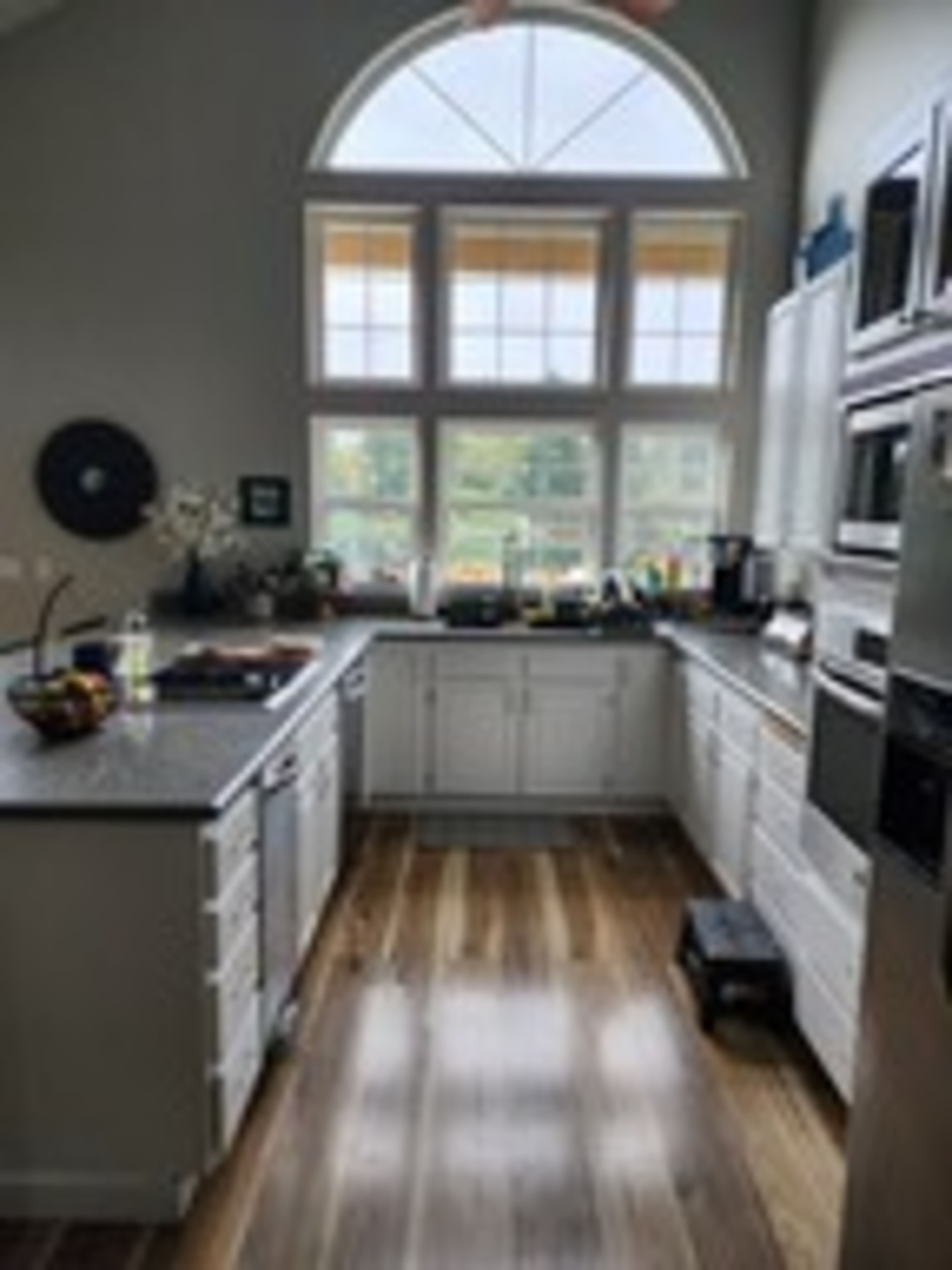 A modern kitchen features white cabinetry, stainless steel appliances, and large windows allowing natural light to illuminate the space.