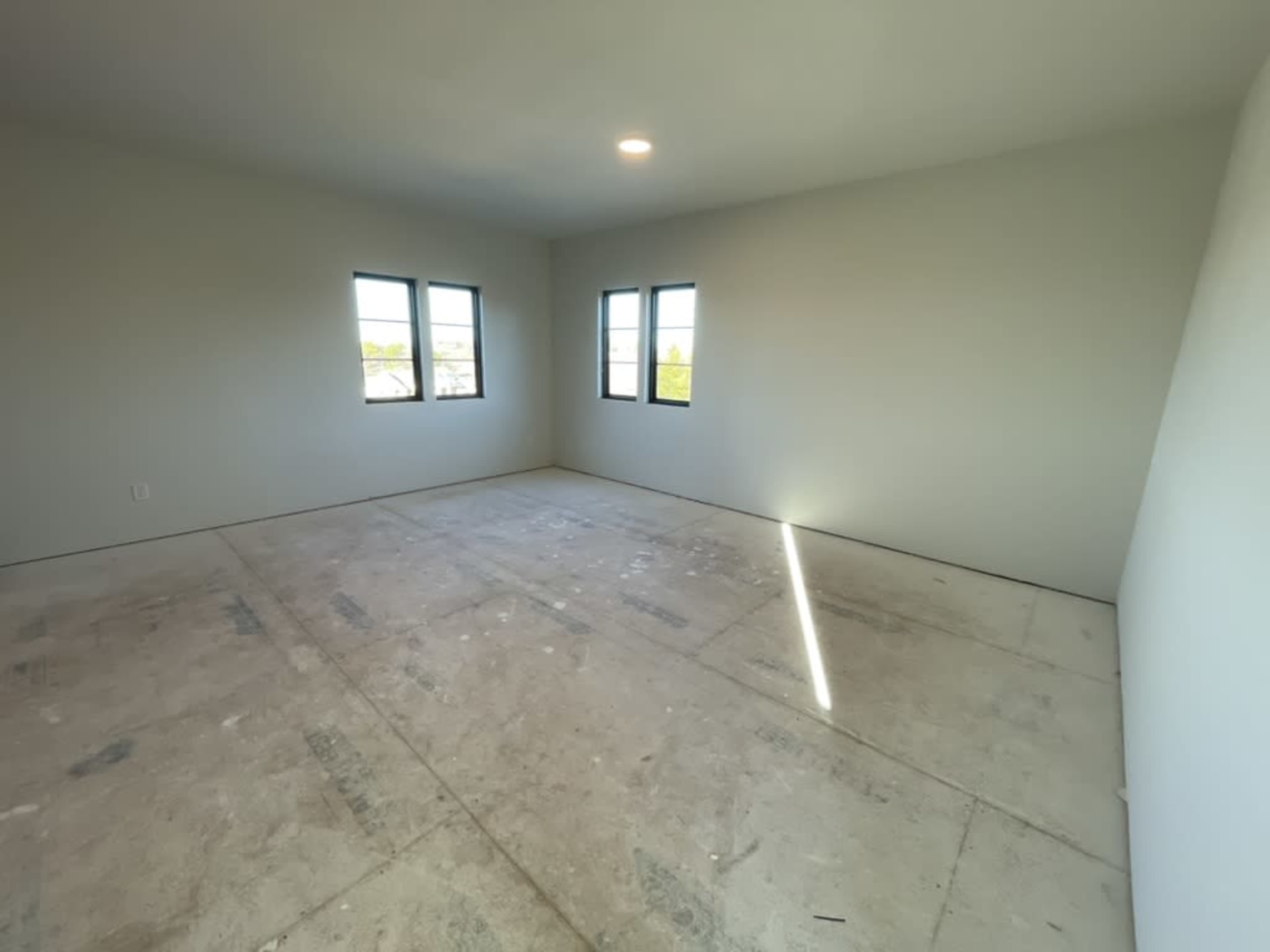 The image shows an empty room with four windows and unfinished flooring.