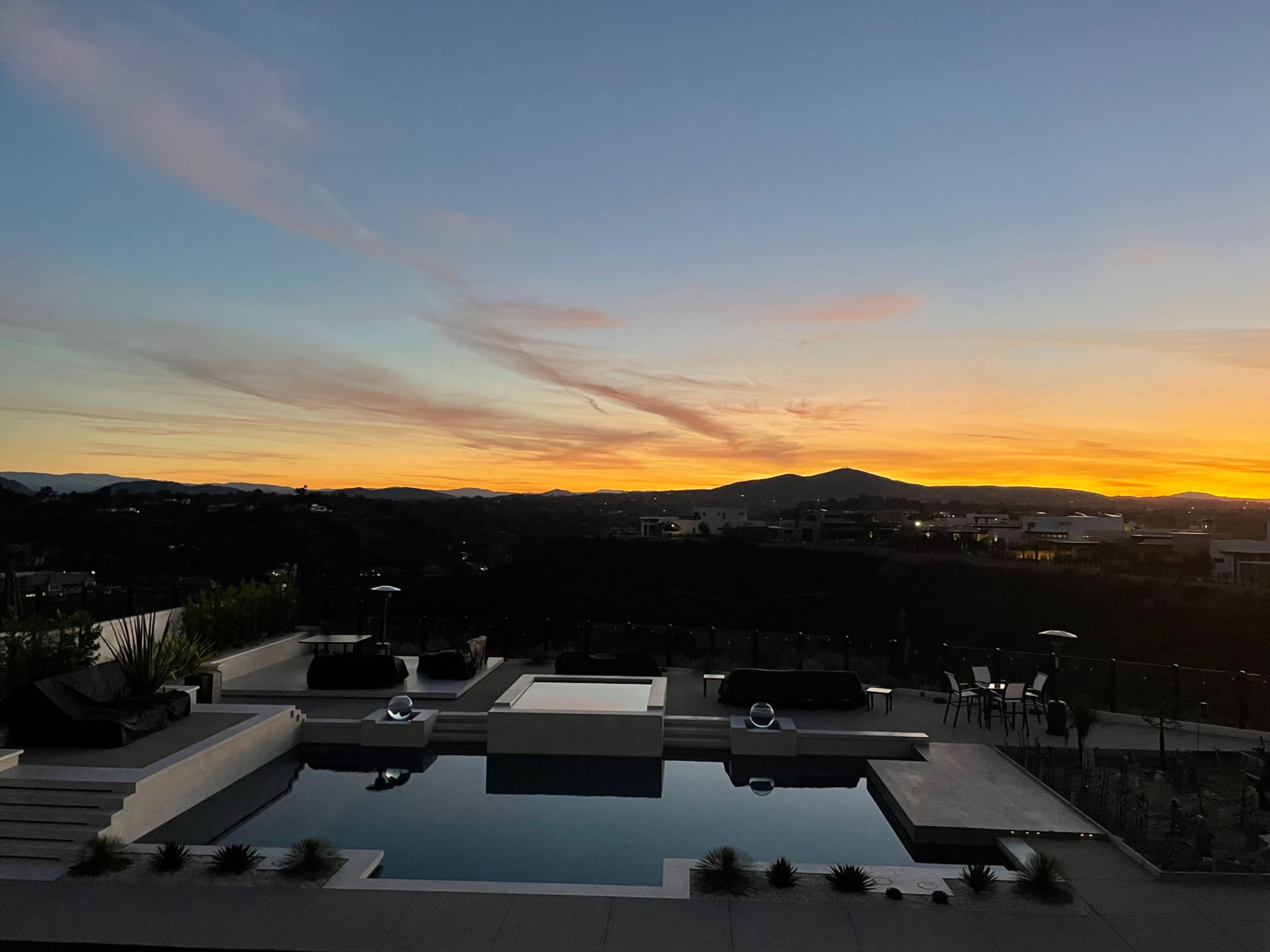A rooftop pool area with modern seating, framed by a vibrant sunset and mountains in the background.