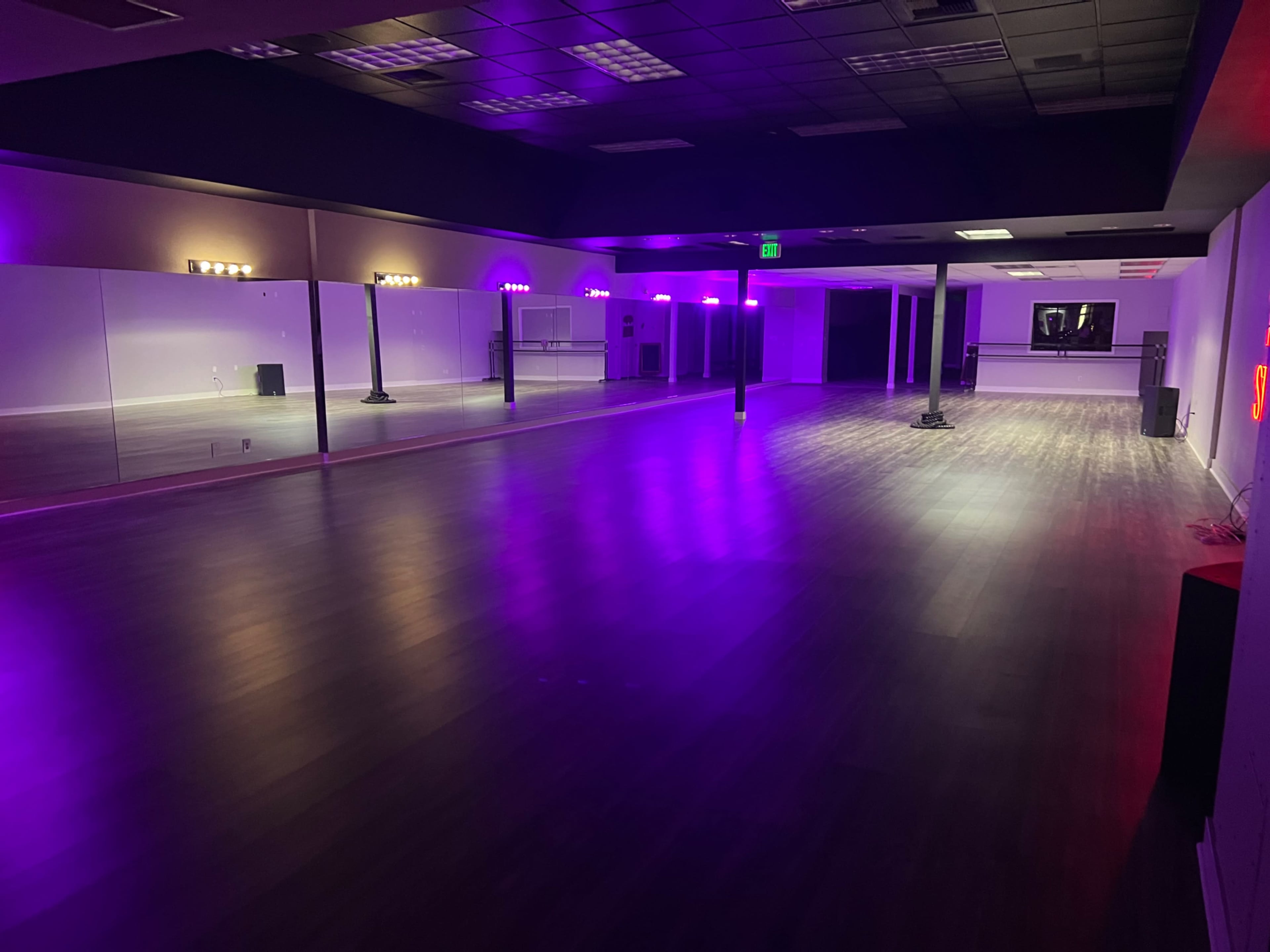 A spacious dance studio with purple lighting and mirrored walls.