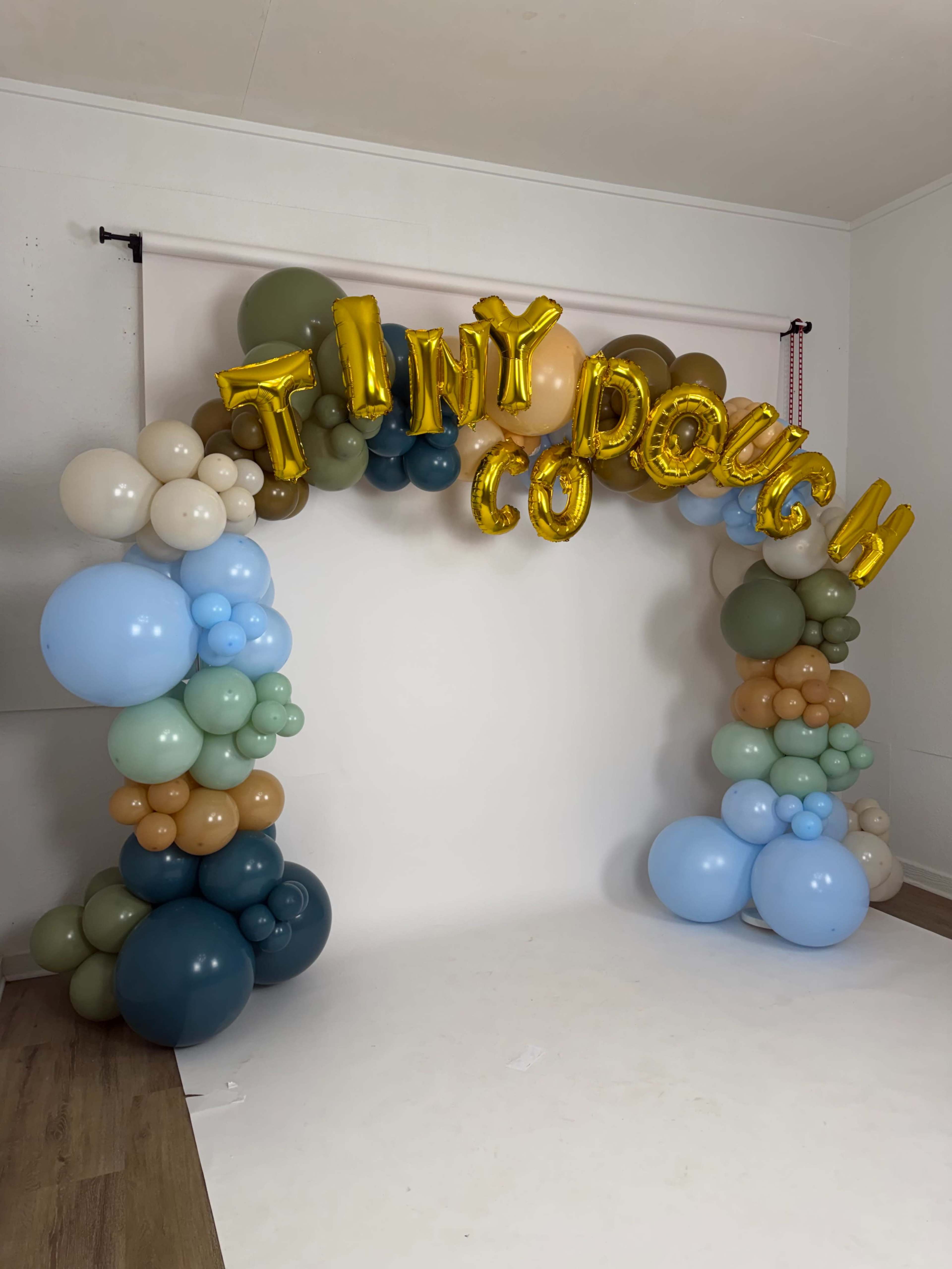 A colorful balloon arch with the words "TINY DOUGH" displayed prominently is set against a white backdrop.