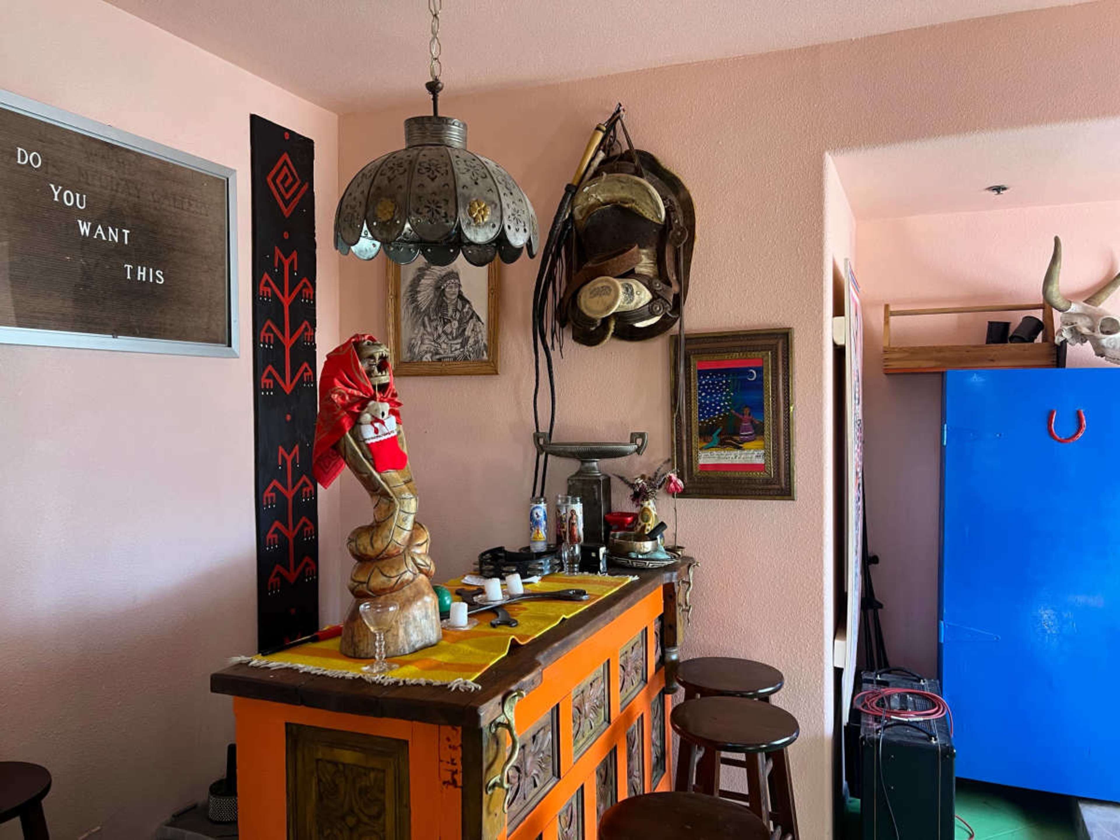 The image shows a vibrant bar area adorned with various decorations, including a lamp, a statue, and a framed picture, set against a pastel-colored wall.