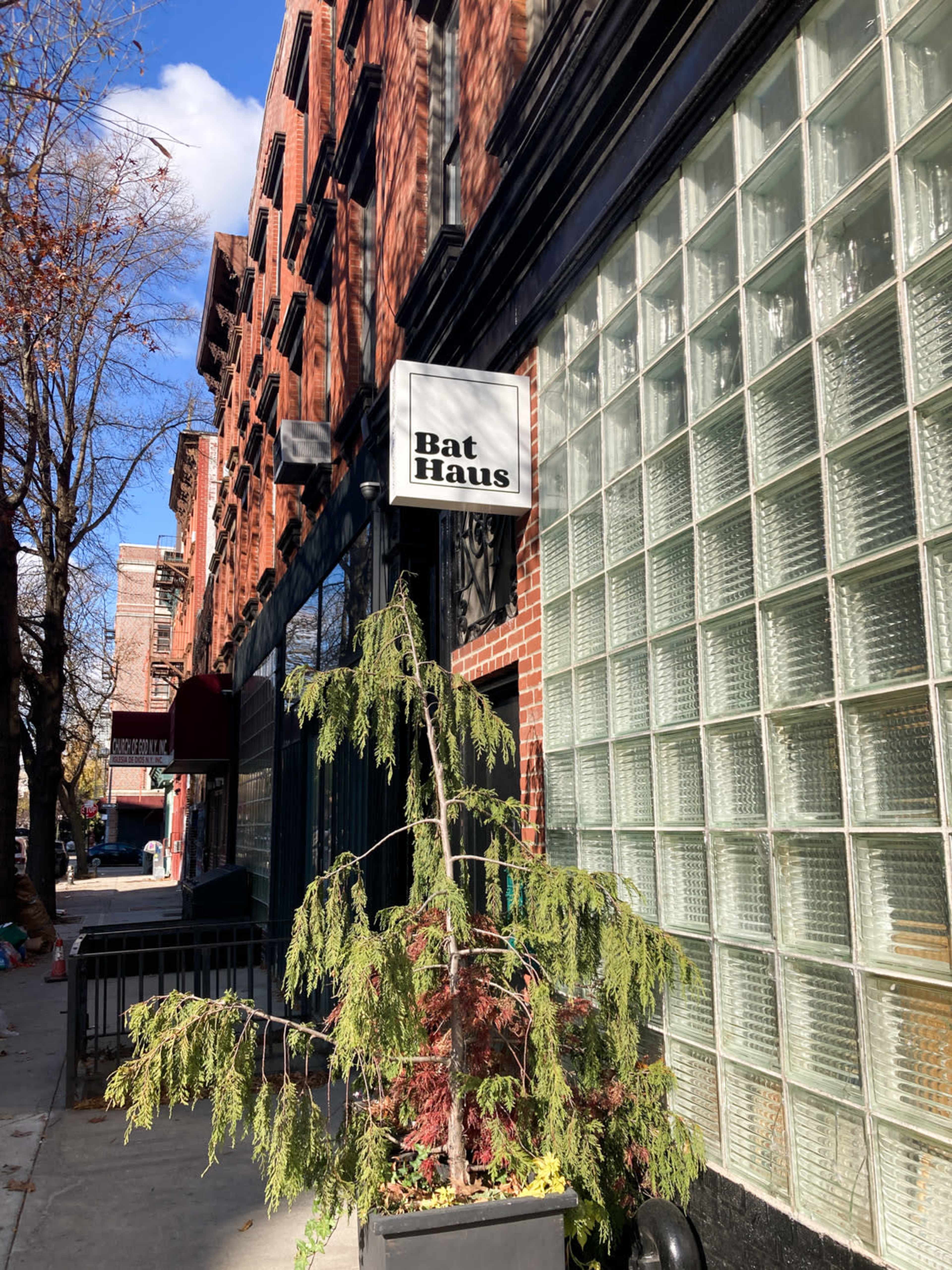 The image shows a brick building on a city street with a sign reading "Bat Haus" and a potted plant near the entrance.