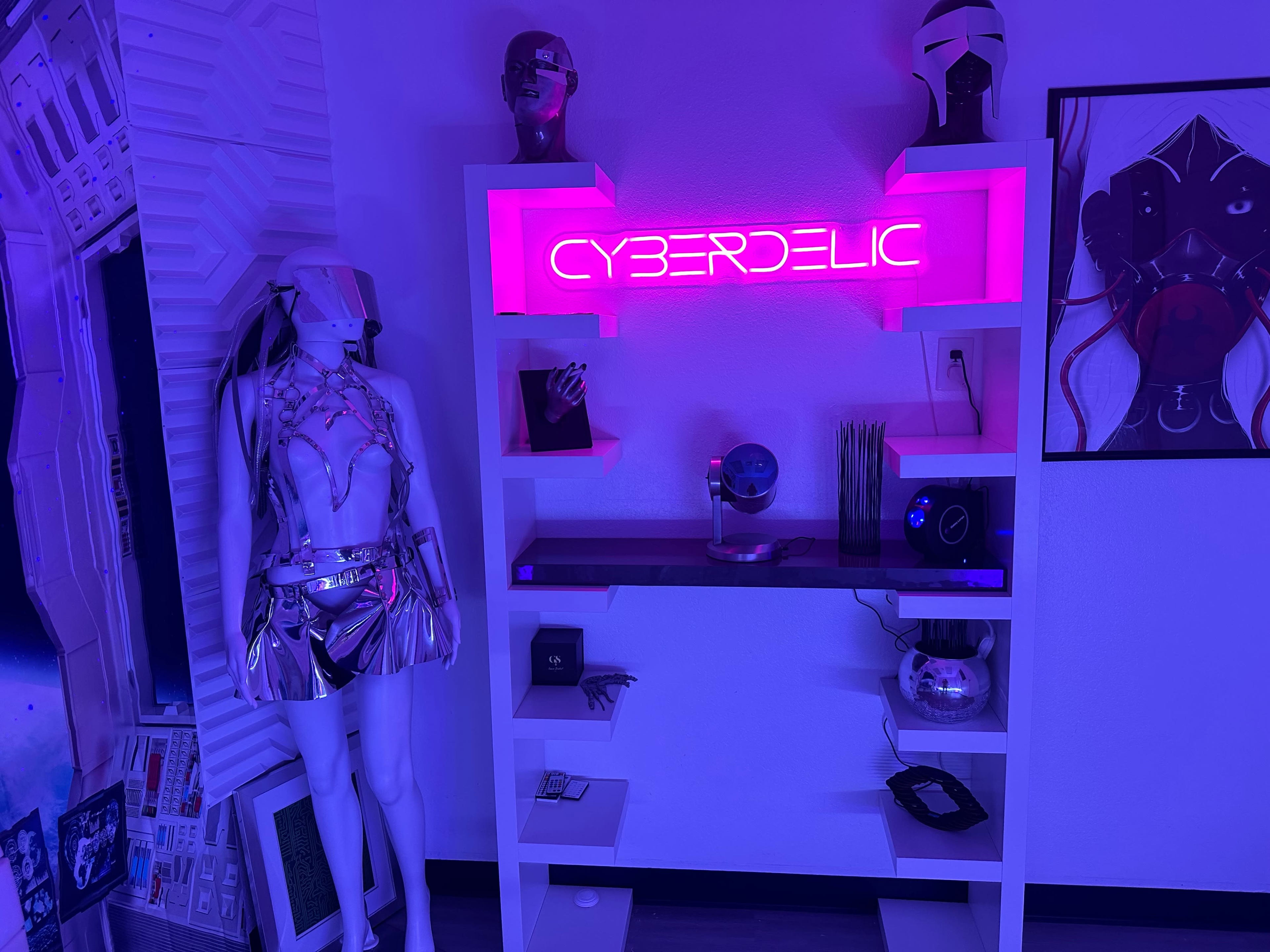 A modern display featuring a neon sign that reads "CYBERDELIC," along with a mannequin dressed in metallic clothing, set against a backdrop of colorful lighting.
