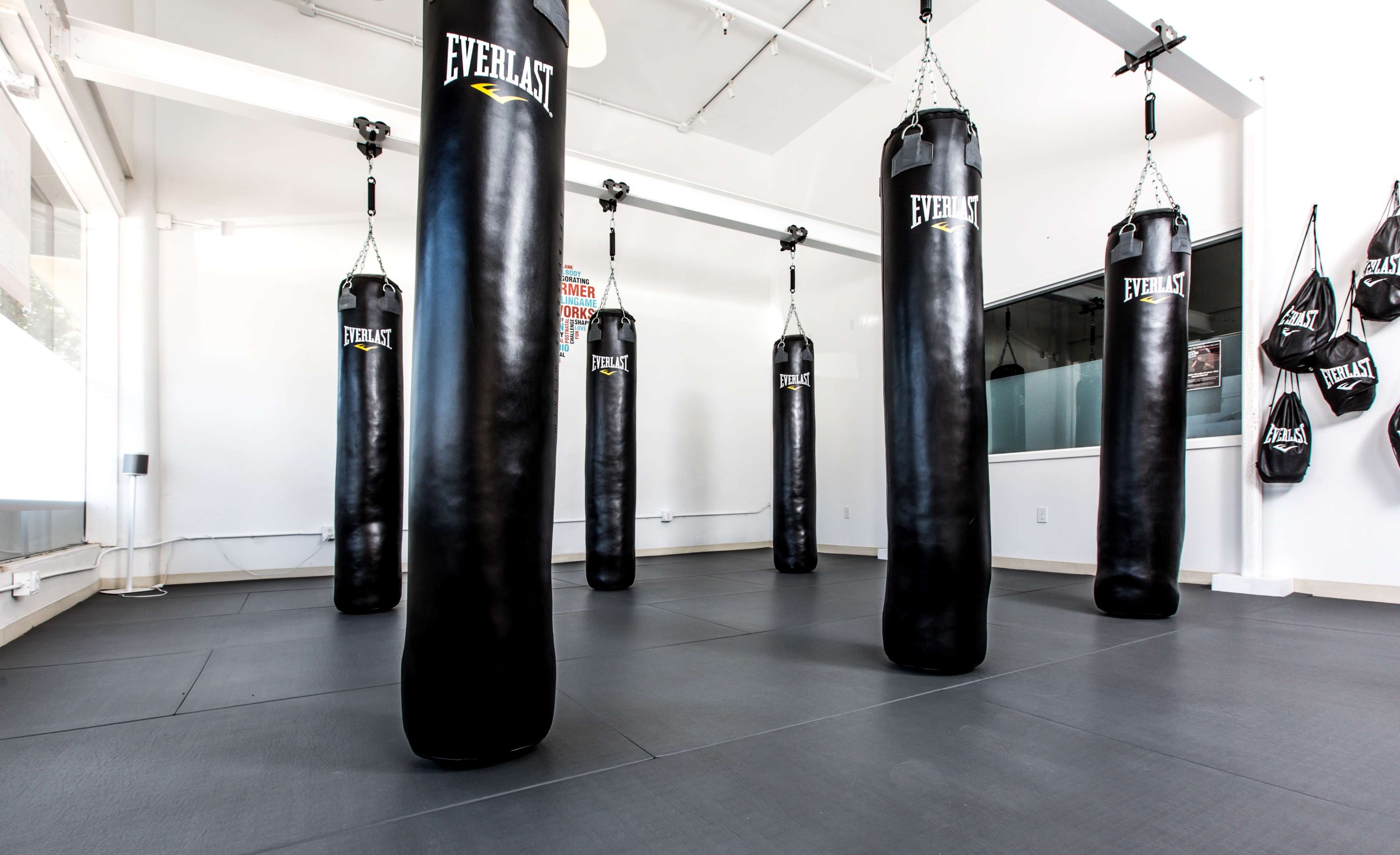 A gym space with multiple black punching bags hanging from the ceiling in a well-lit room.